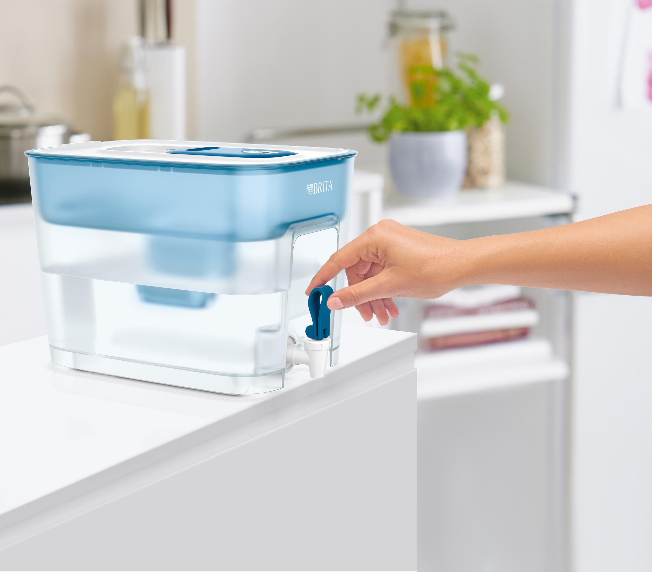 A hand operates the blue tap on a Brita water filter on a white countertop.