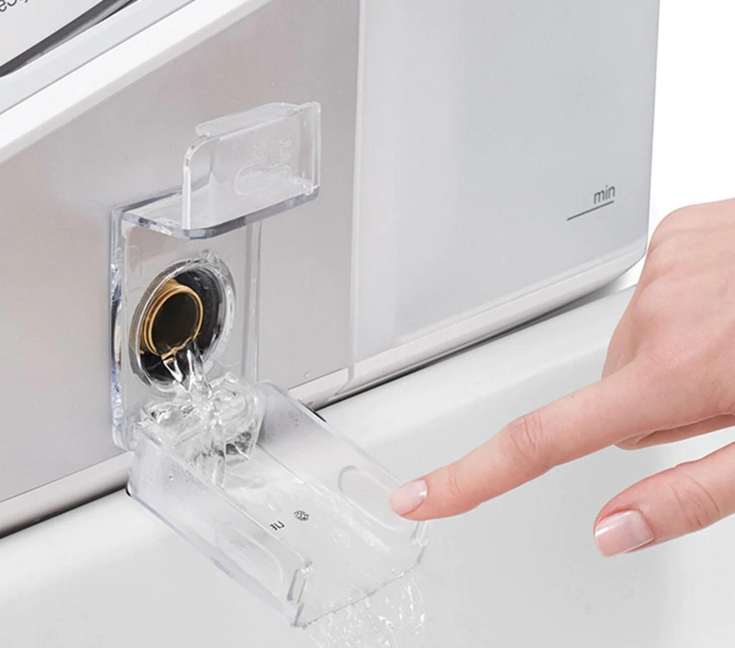 El agua fluye de un dispensador transparente a un cajón debajo. Una mano lo señala.