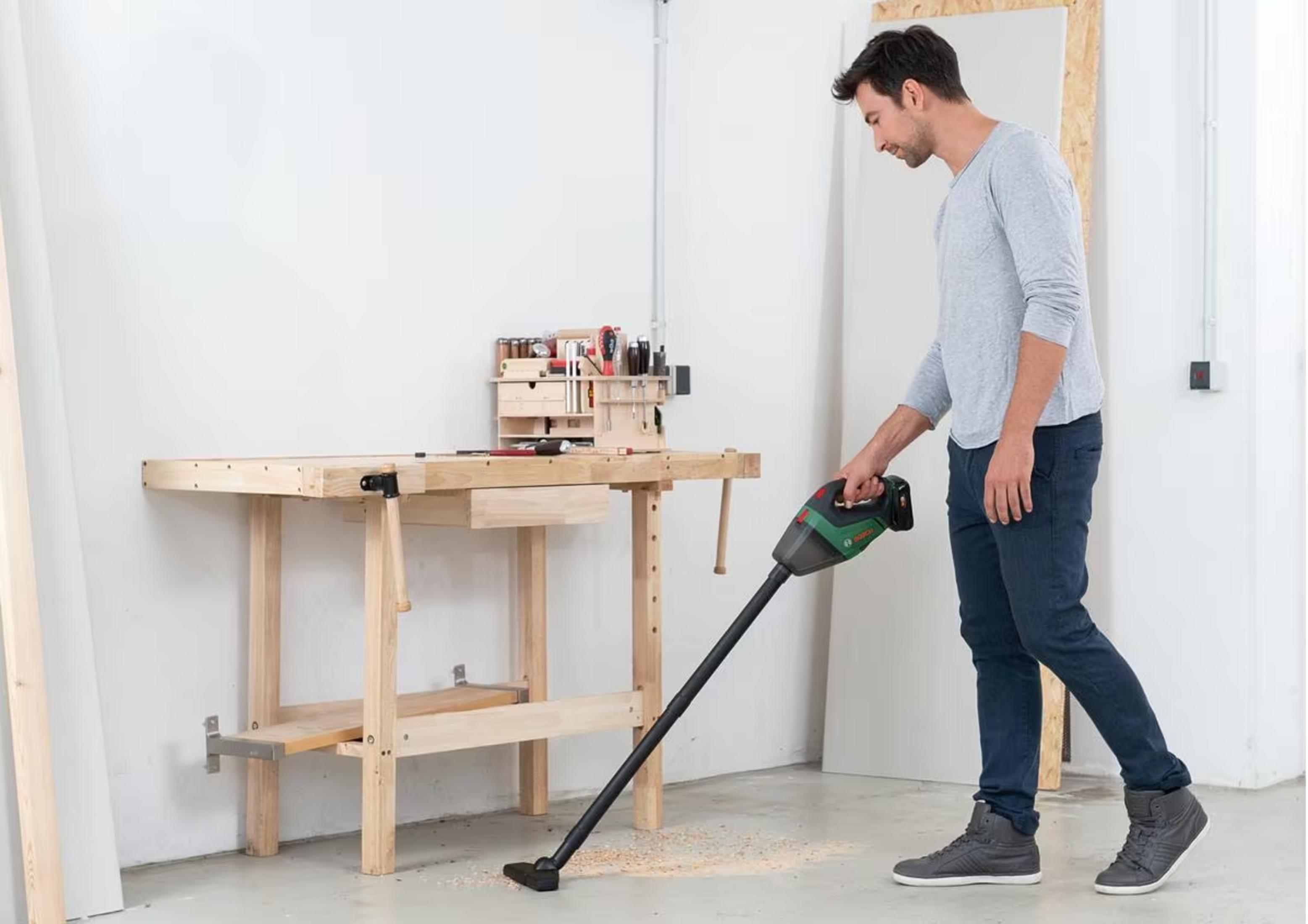 Hombre aspira virutas de madera con aspiradora de mano en taller.