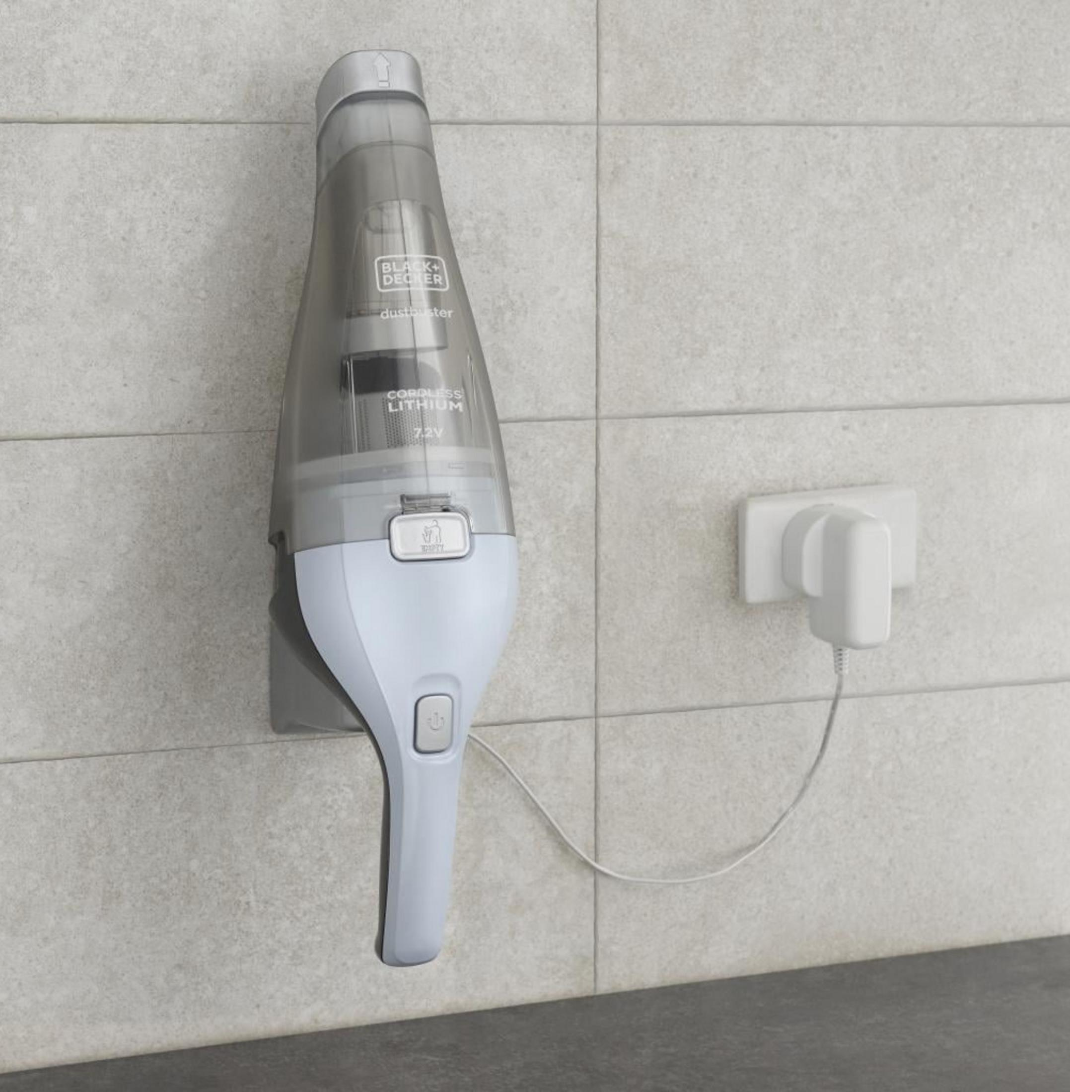 Un aspirateur à main gris se charge sur un chargeur mural.
