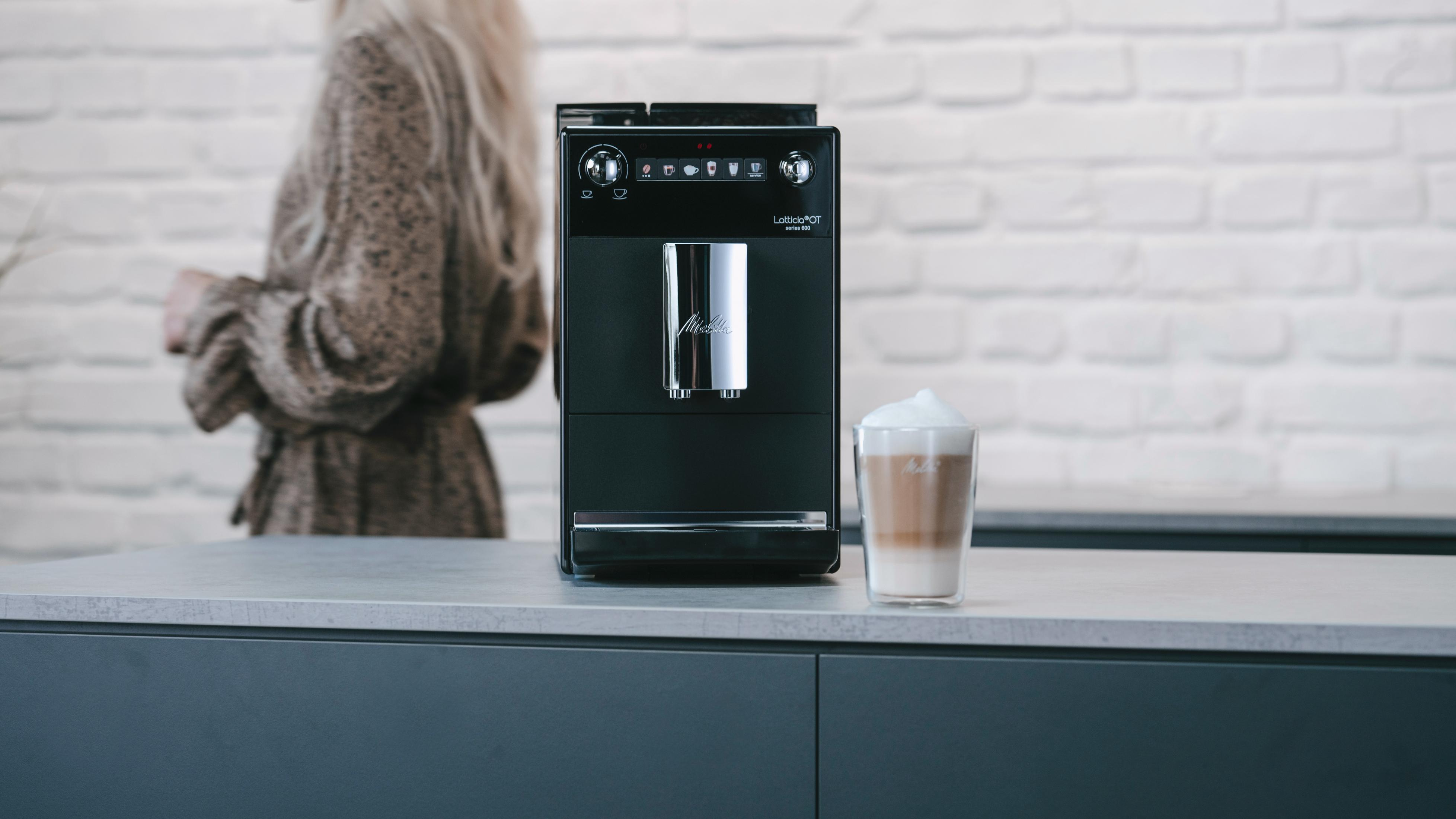 Una macchina da caffè nera con un bicchiere di latte montato accanto.