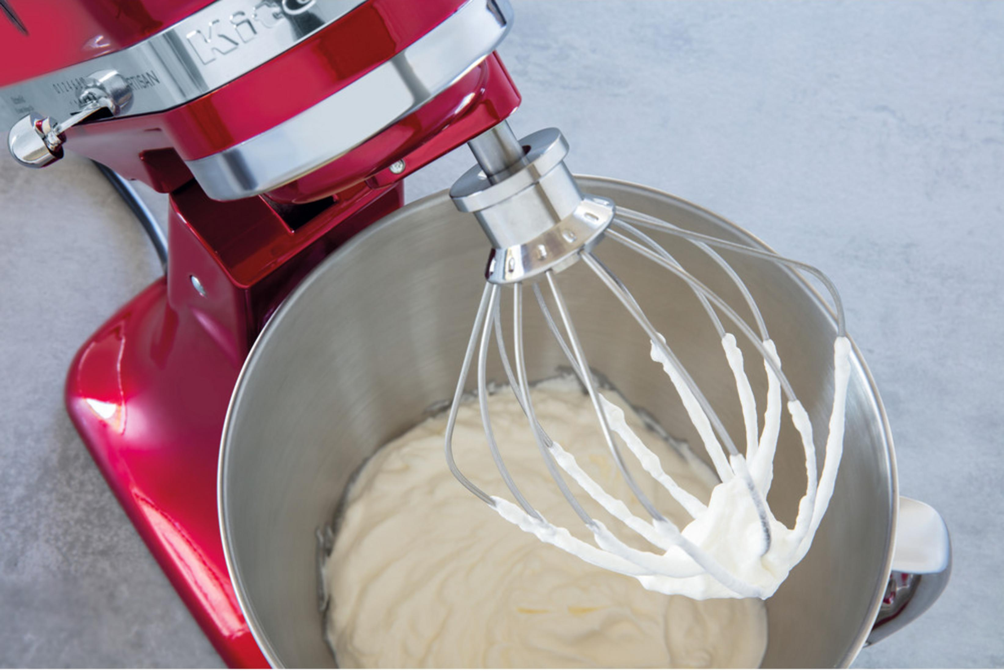 Ein roter Küchenmixer mit Schneebesen, der Sahne in einer Edelstahlschüssel schlägt.