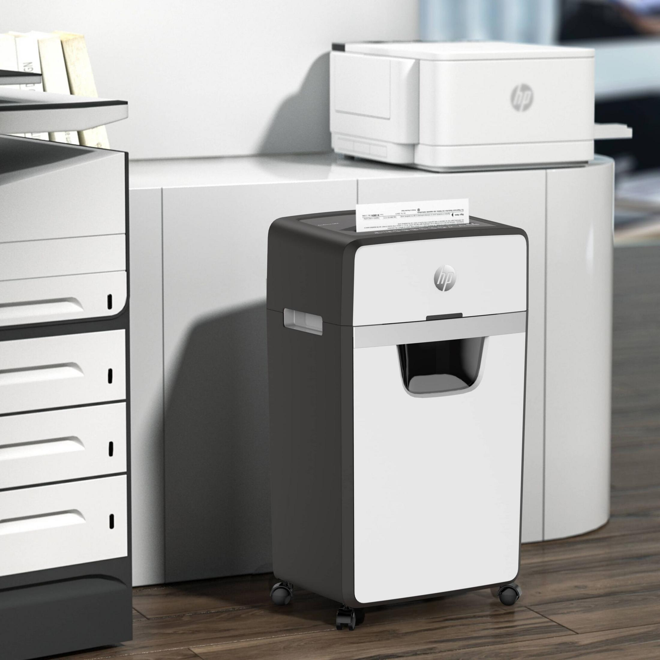 Un distruggidocumenti HP bianco e nero su ruote è accanto a una stampante e un archivio.