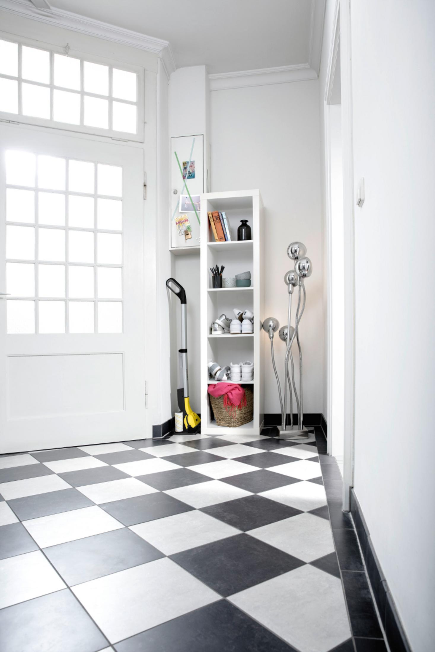 Corridoio con pavimento a scacchiera, porta bianca, scaffale con scarpe e decorazioni.