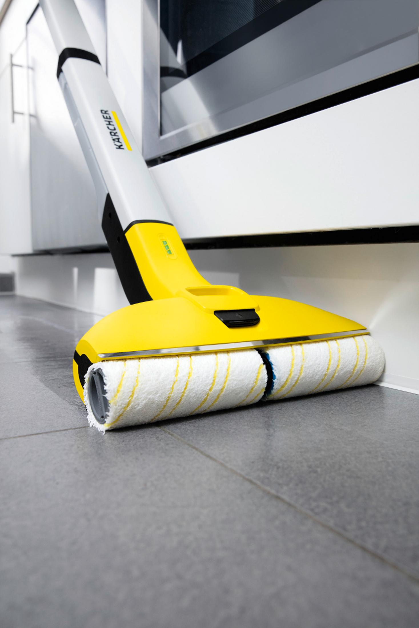 Un pulitore per pavimenti Karcher giallo con due rulli su un pavimento piastrellato grigio.