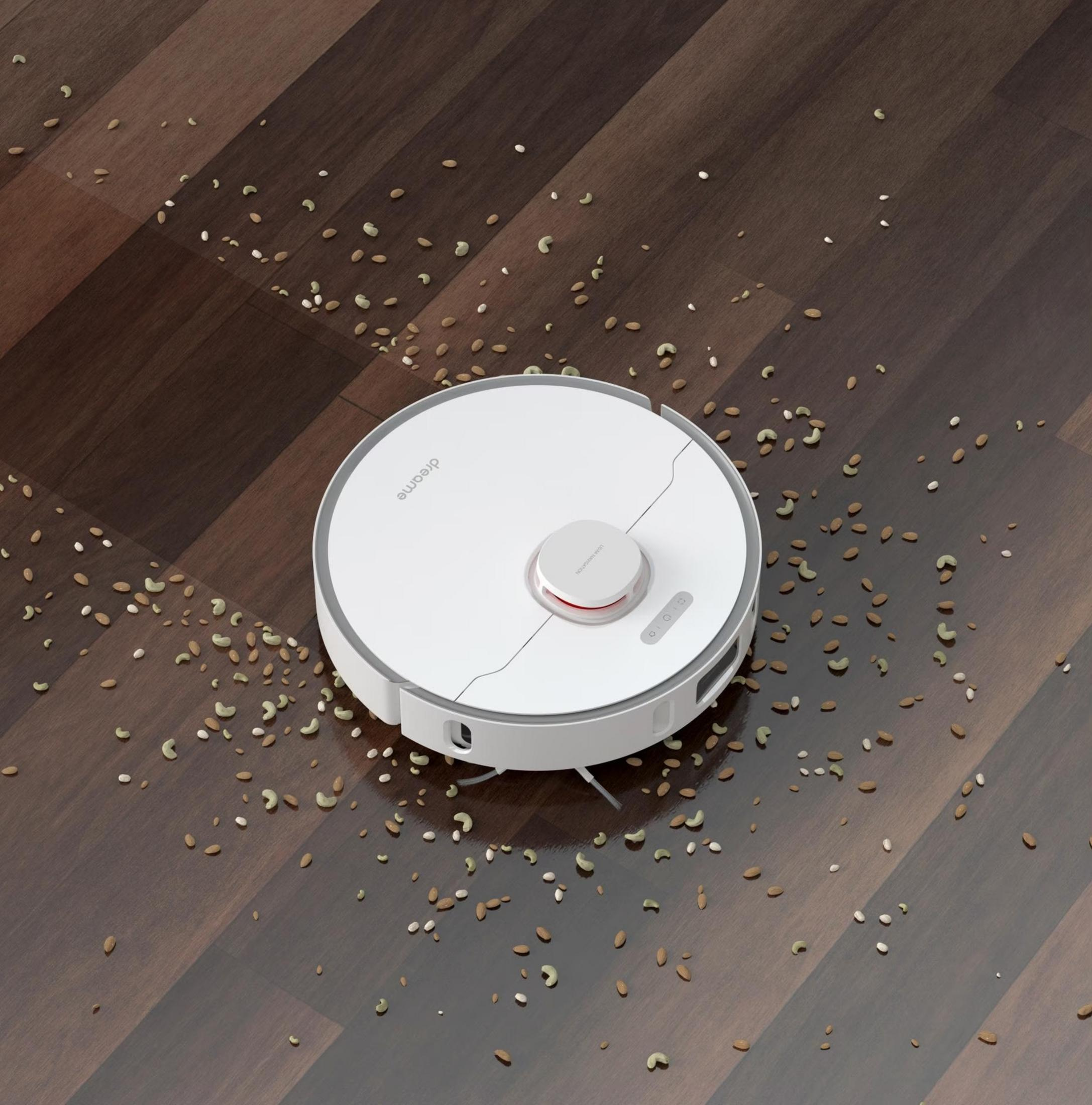 Un aspirateur robot blanc sur un parquet avec des noix éparpillées.