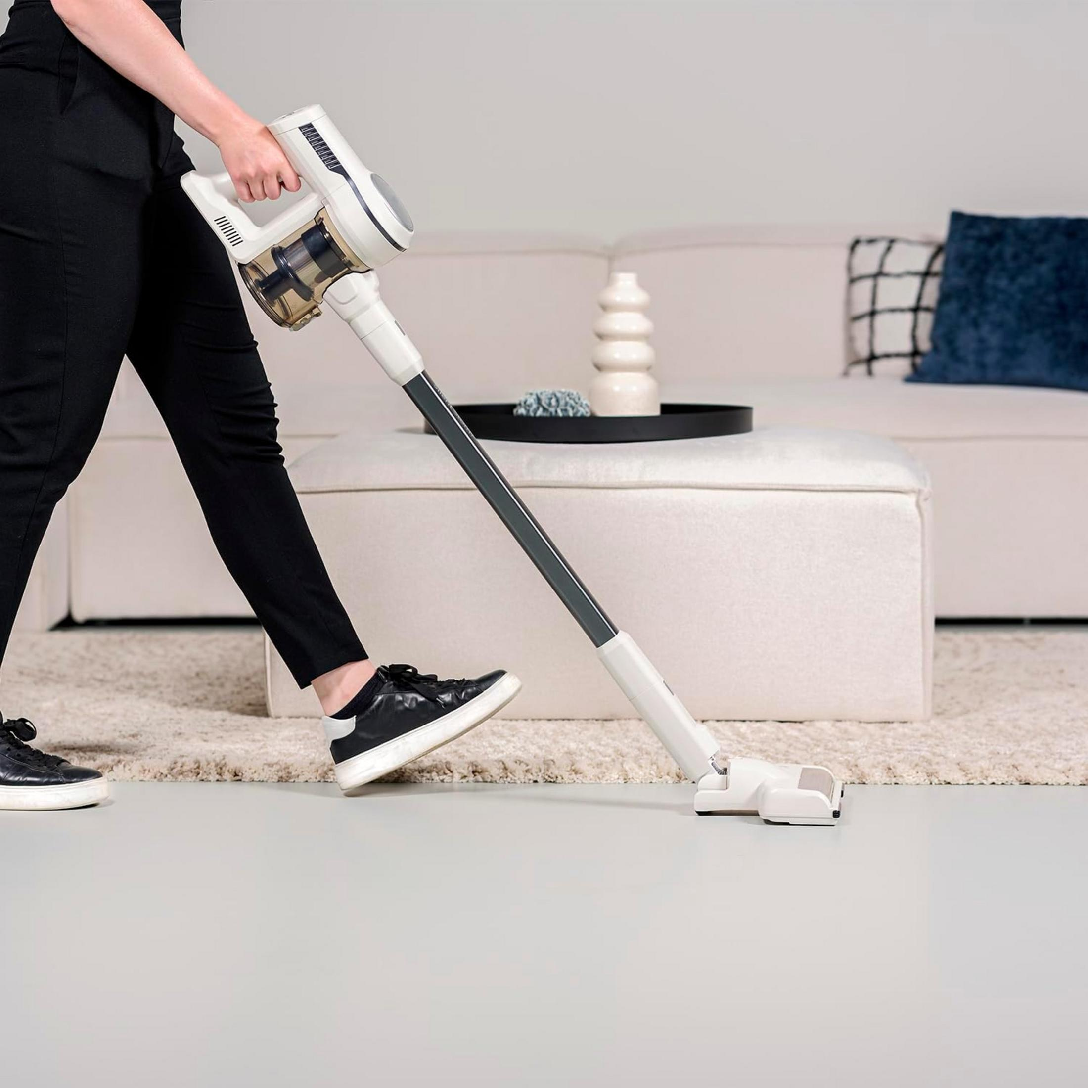 Una persona aspira con un aspirapolvere portatile bianco su un pavimento grigio.