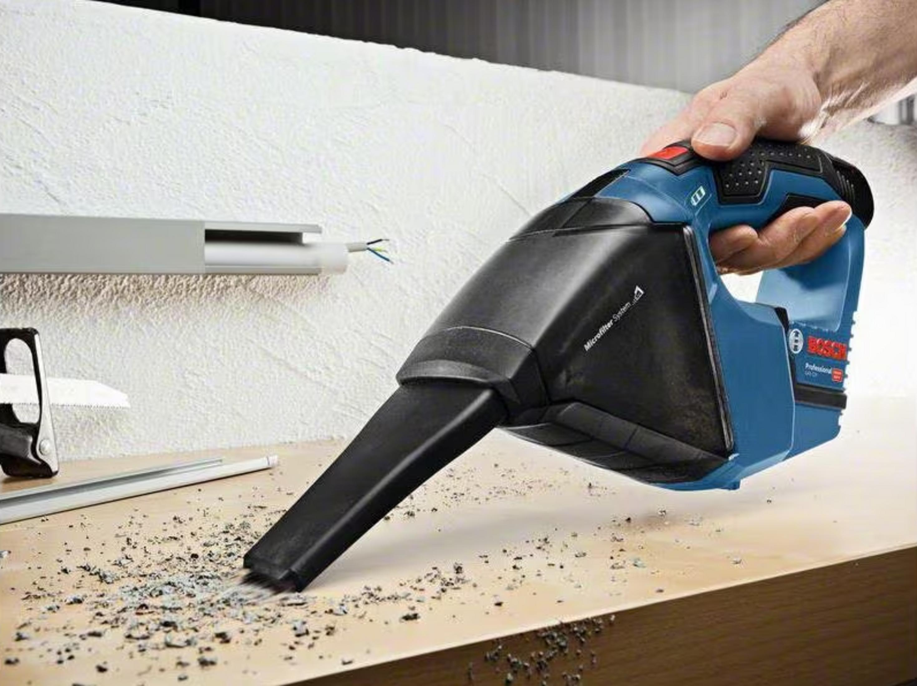 Un homme tient un aspirateur Bosch bleu, aspirant des débris.