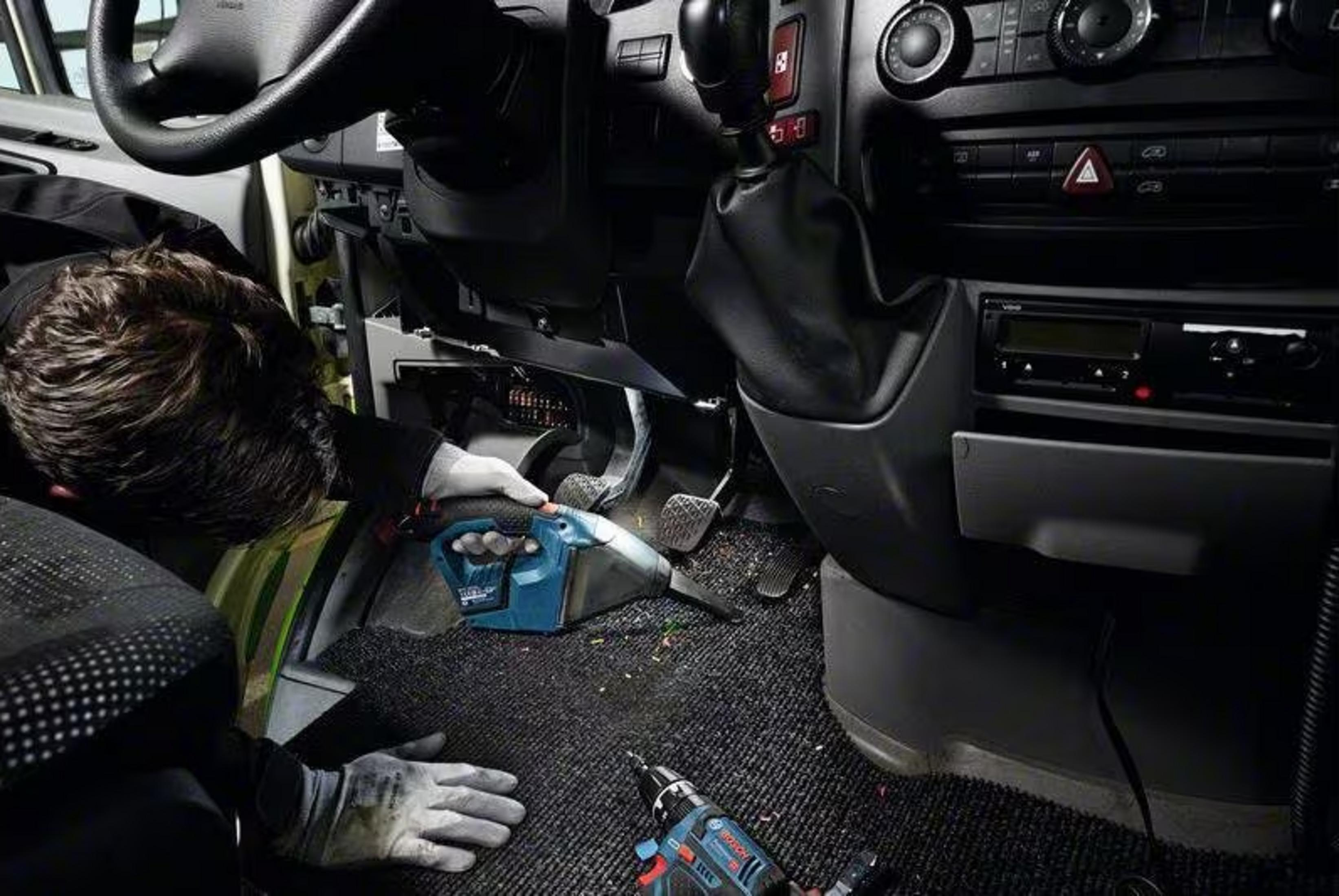 Homme nettoie l'intérieur d'un camion avec aspirateur bleu.