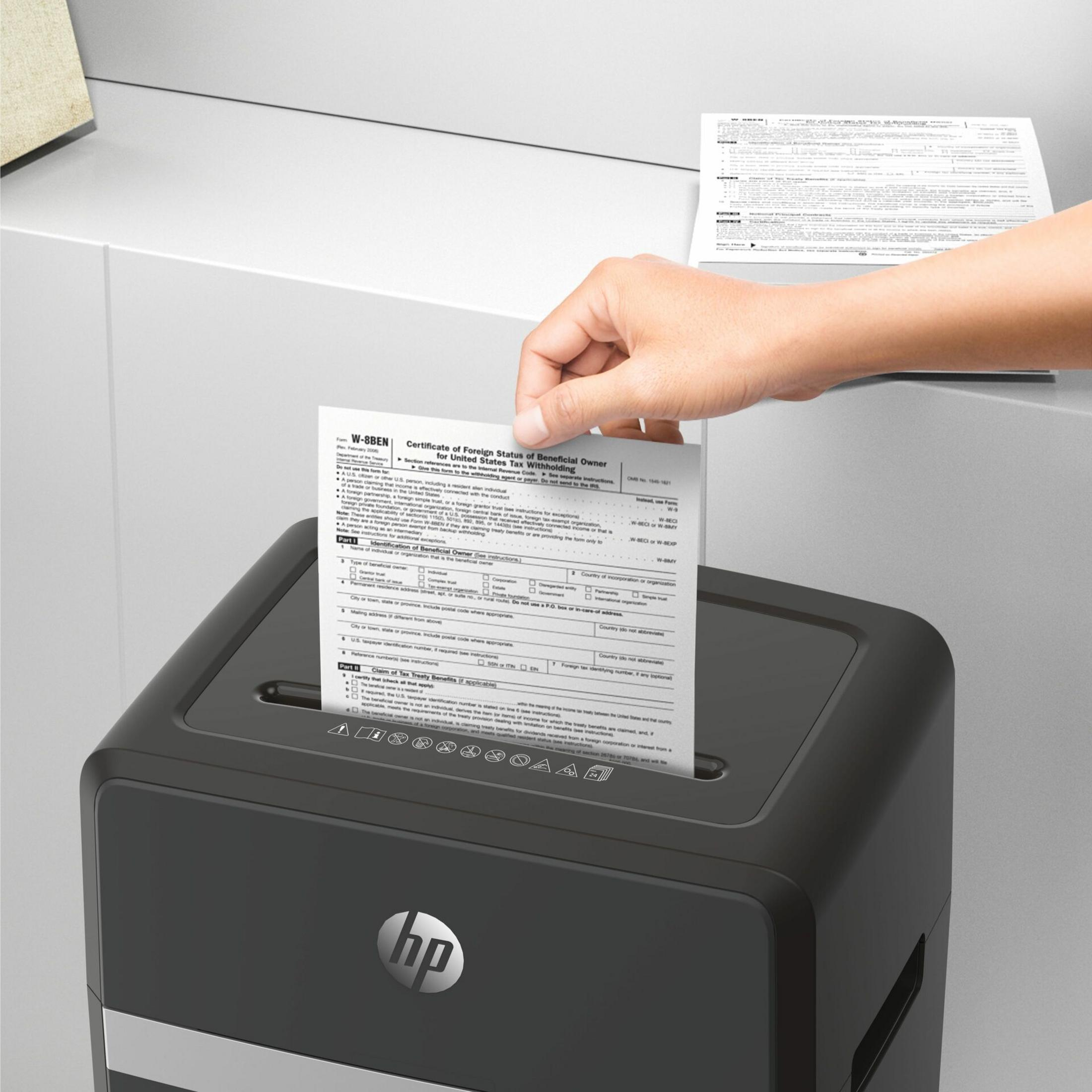 Una mano inserisce un modulo W-8BEN in un distruggi documenti con logo HP.