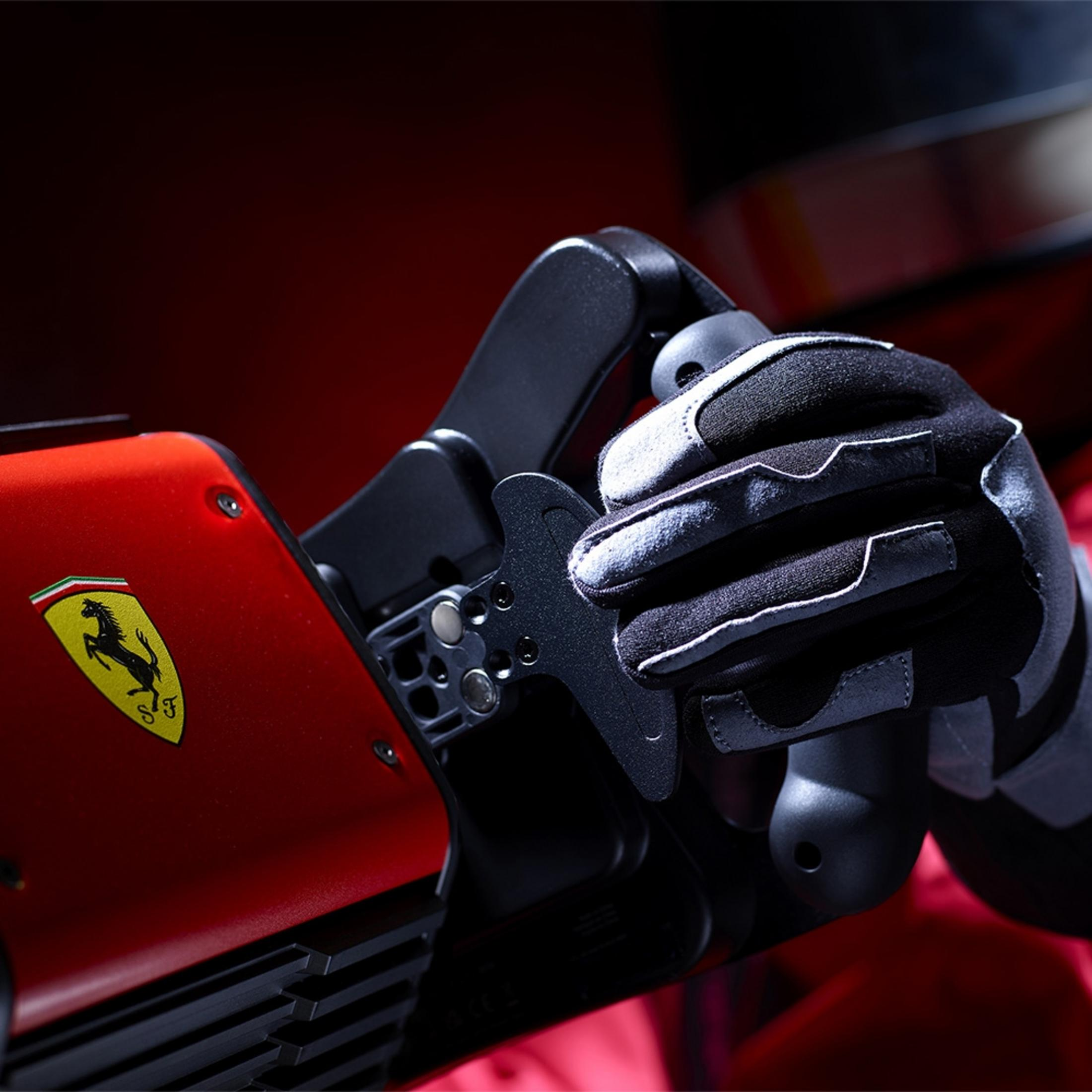 Ręka w rękawicy trzyma czerwony kierownicę z logo Ferrari. Kontekst wyścigów.