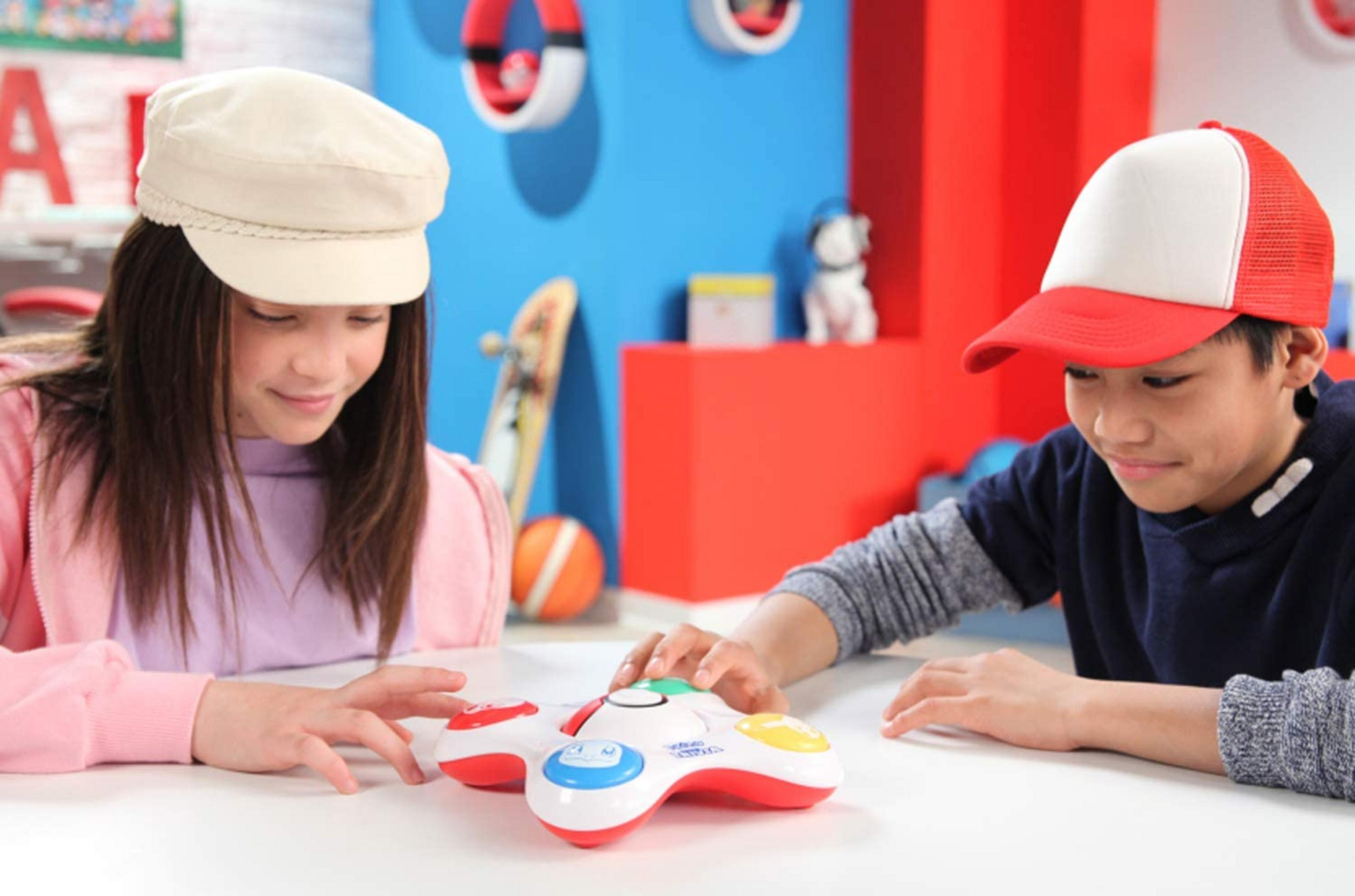 Zwei Kinder spielen mit einem bunten Spielzeugcontroller auf einem weißen Tisch.