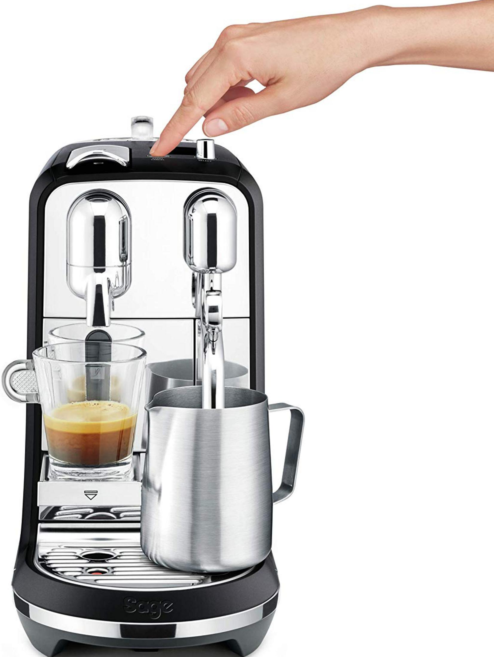 Eine Hand drückt einen Knopf an einer Espressomaschine mit einer Tasse Espresso und einem Milchkännchen.