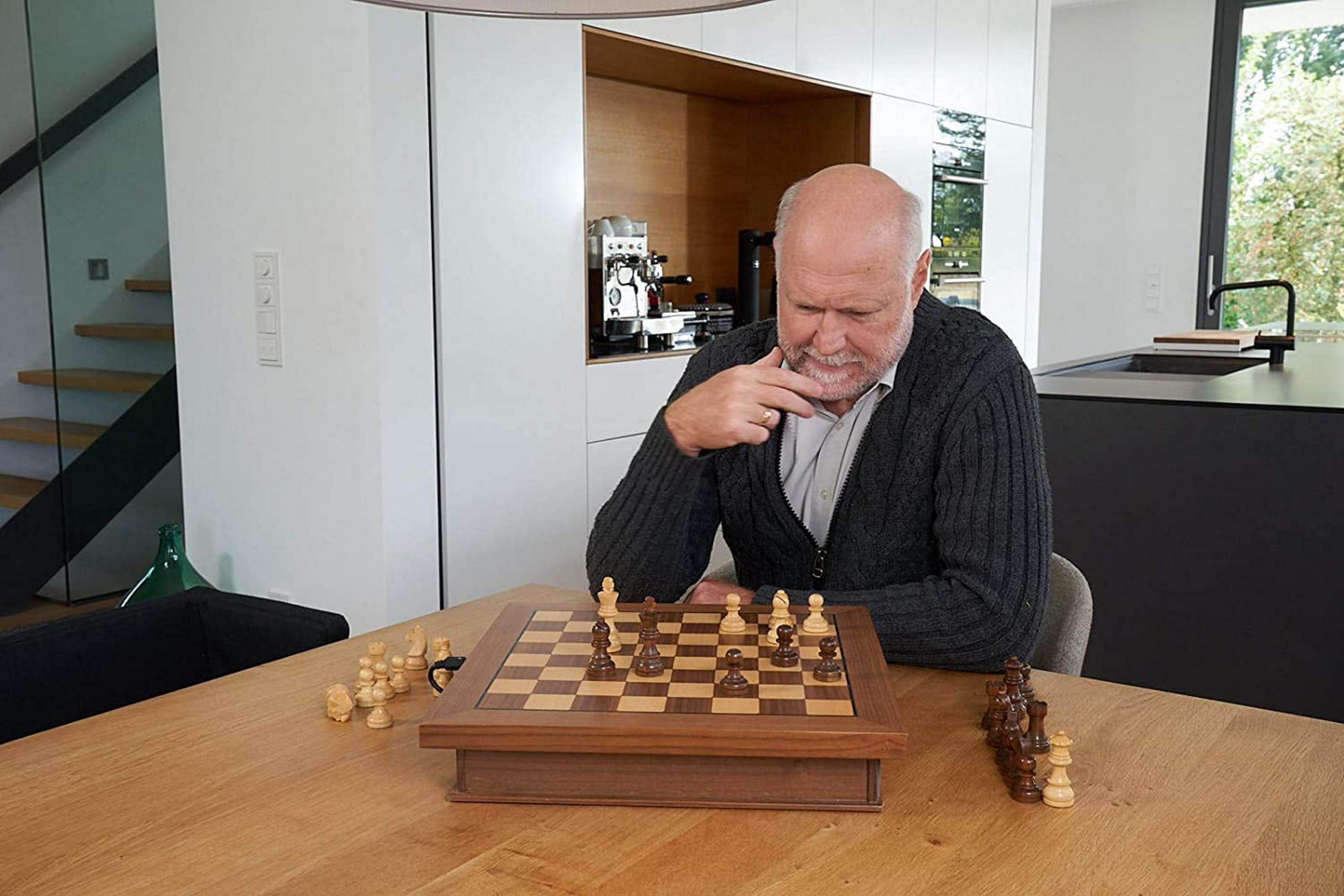 Ein älterer Mann sitzt an einem Tisch und spielt Schach. Ein Schachbrett steht vor ihm.
