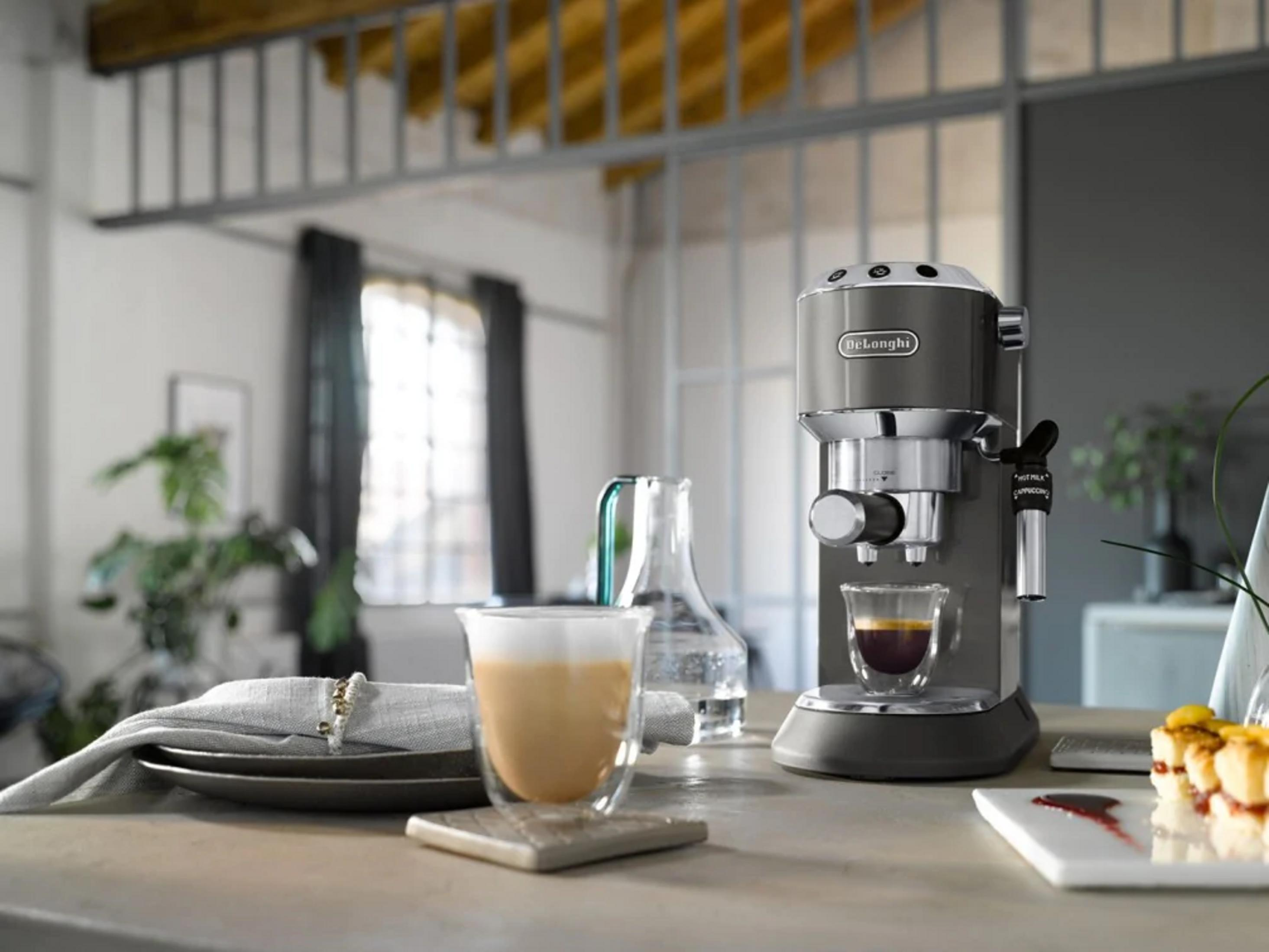 Una cafetera espresso gris prepara café en un vaso junto a un latte.