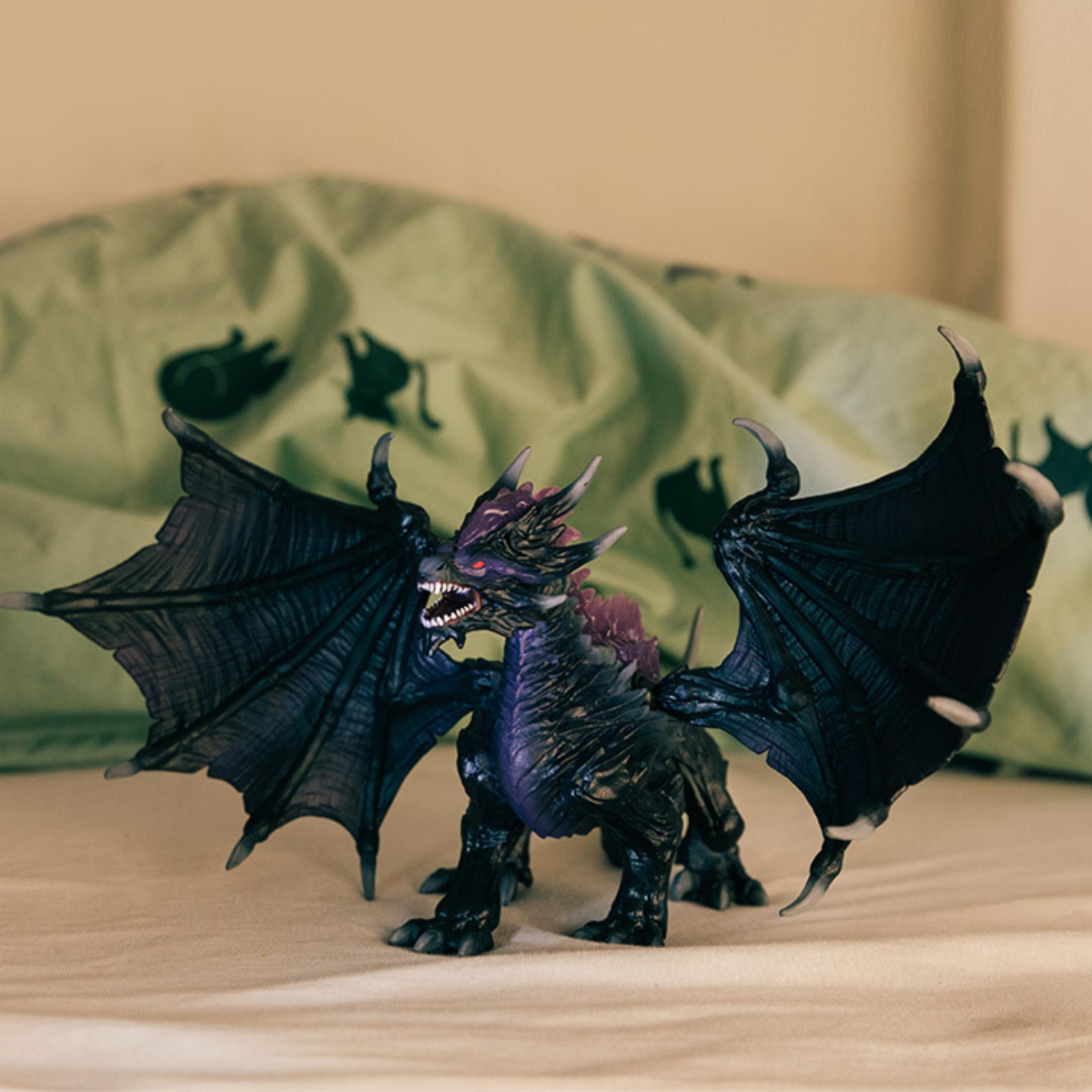 Una figura di drago giocattolo scuro con ali e occhi rossi su una coperta.