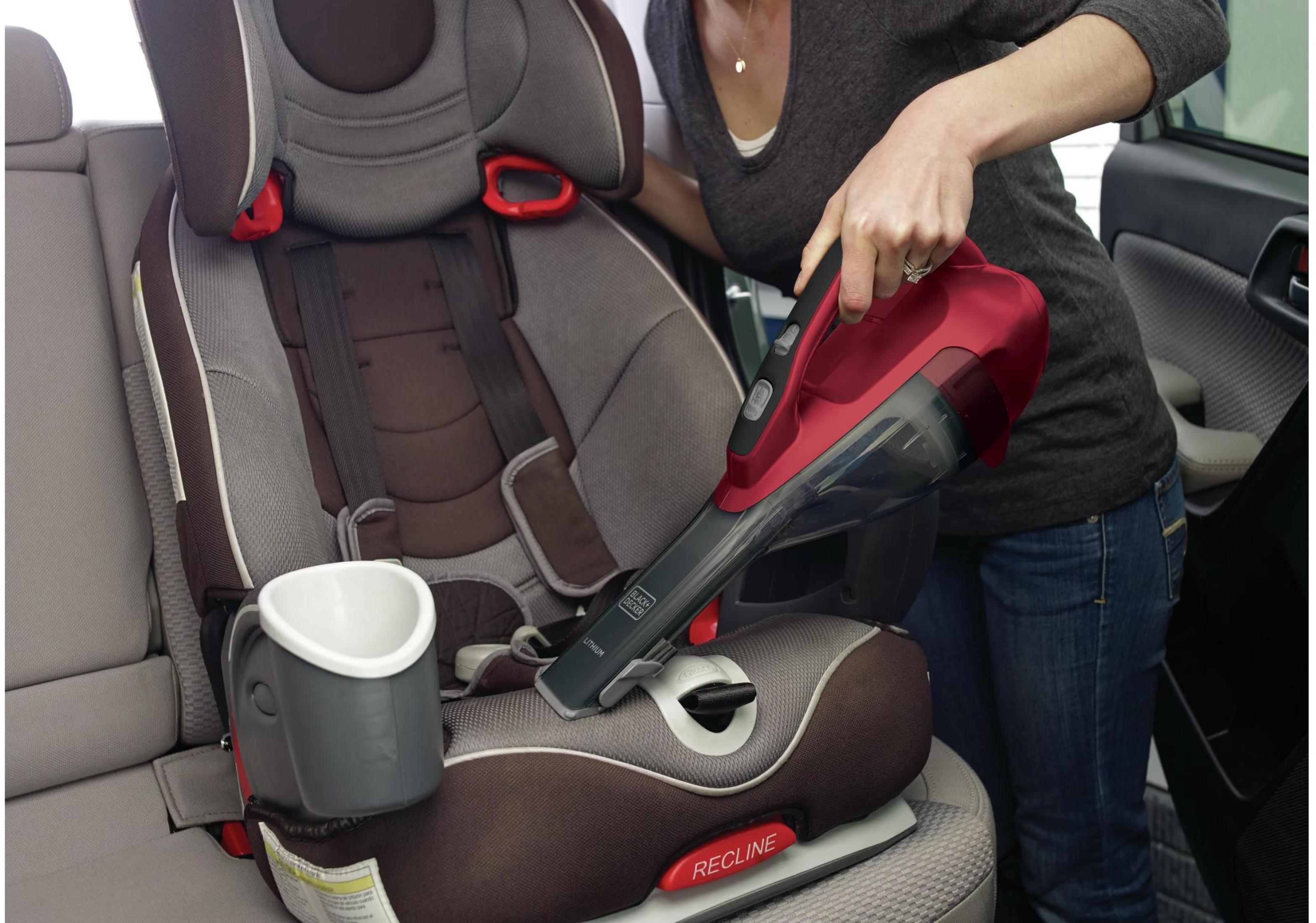 Persona aspira asiento de coche con aspiradora roja de mano.