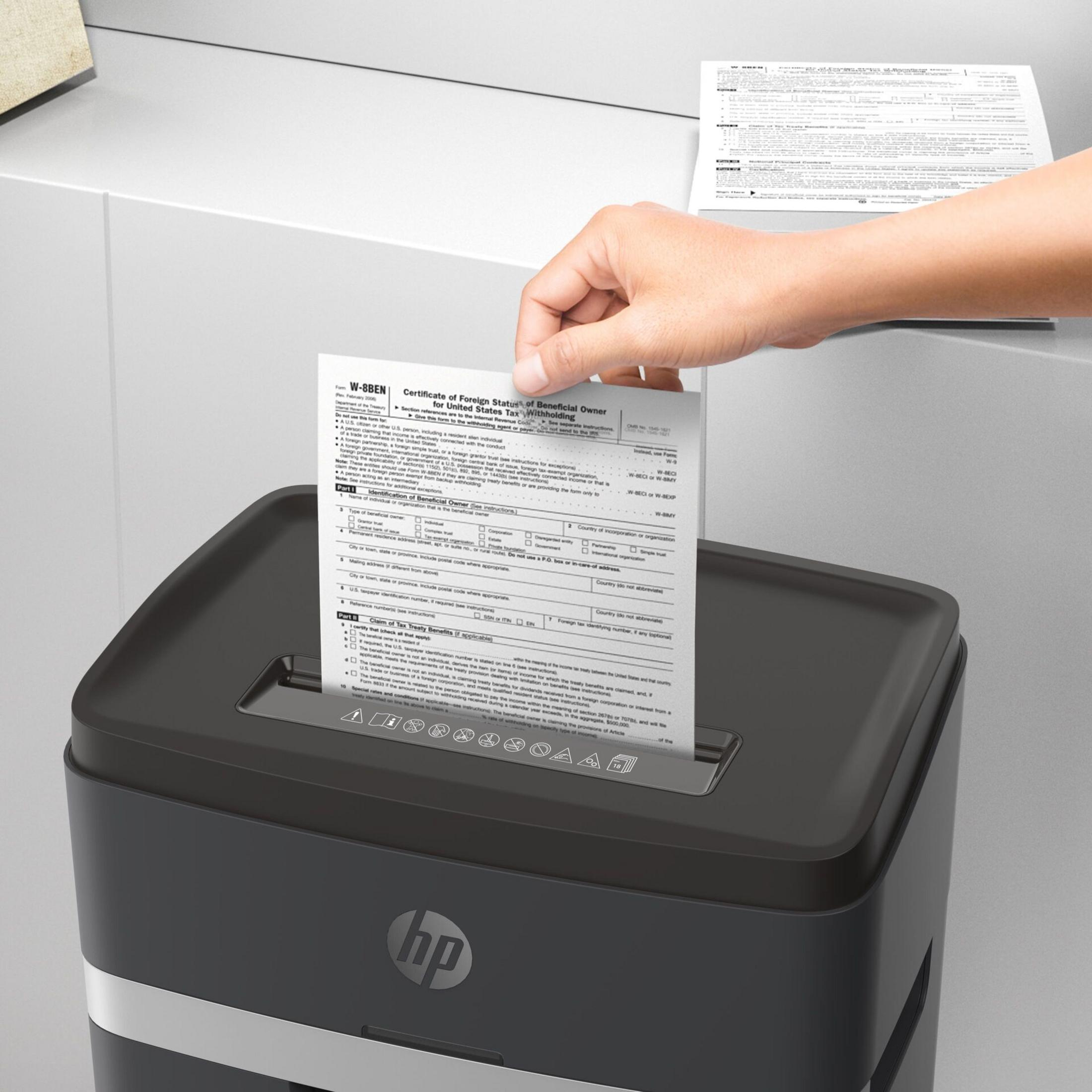 Una mano inserisce un modulo W-8BEN in un distruggi documenti nero.