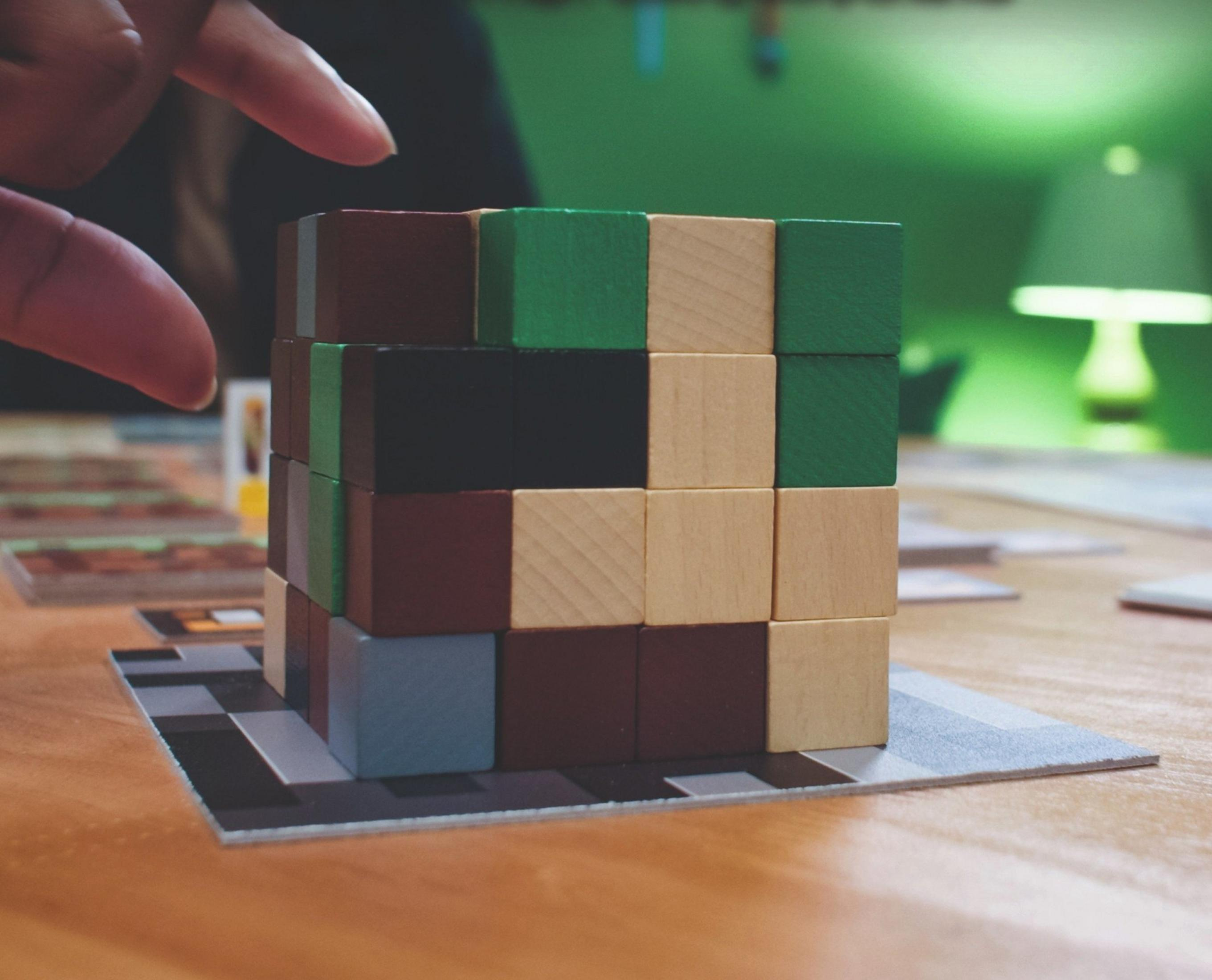 Kolorowe drewniane klocki ułożone na karcie, ręka je przesuwa.