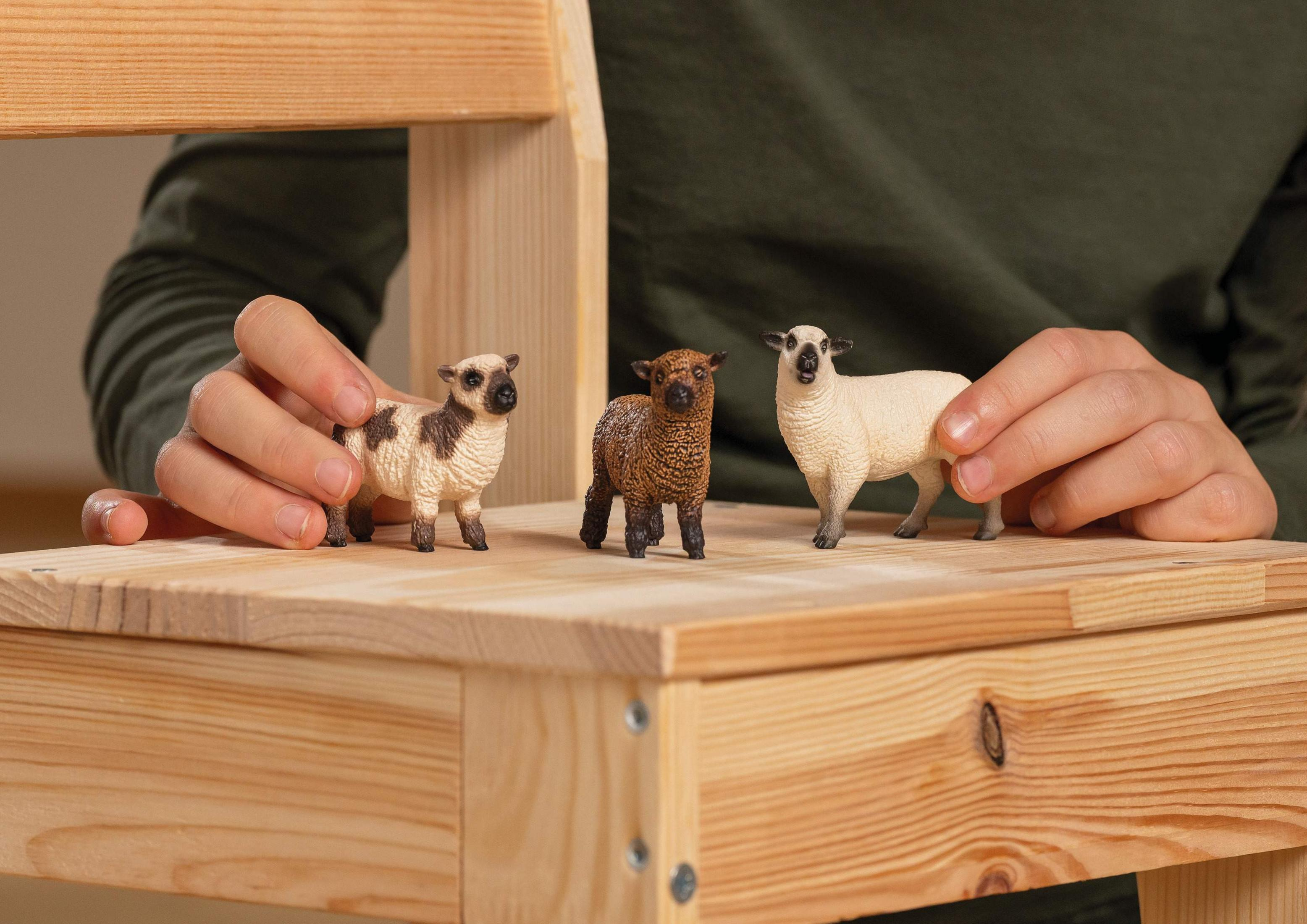 Trzy zabawki owce na drewnianym krześle, trzymane przez ręce.