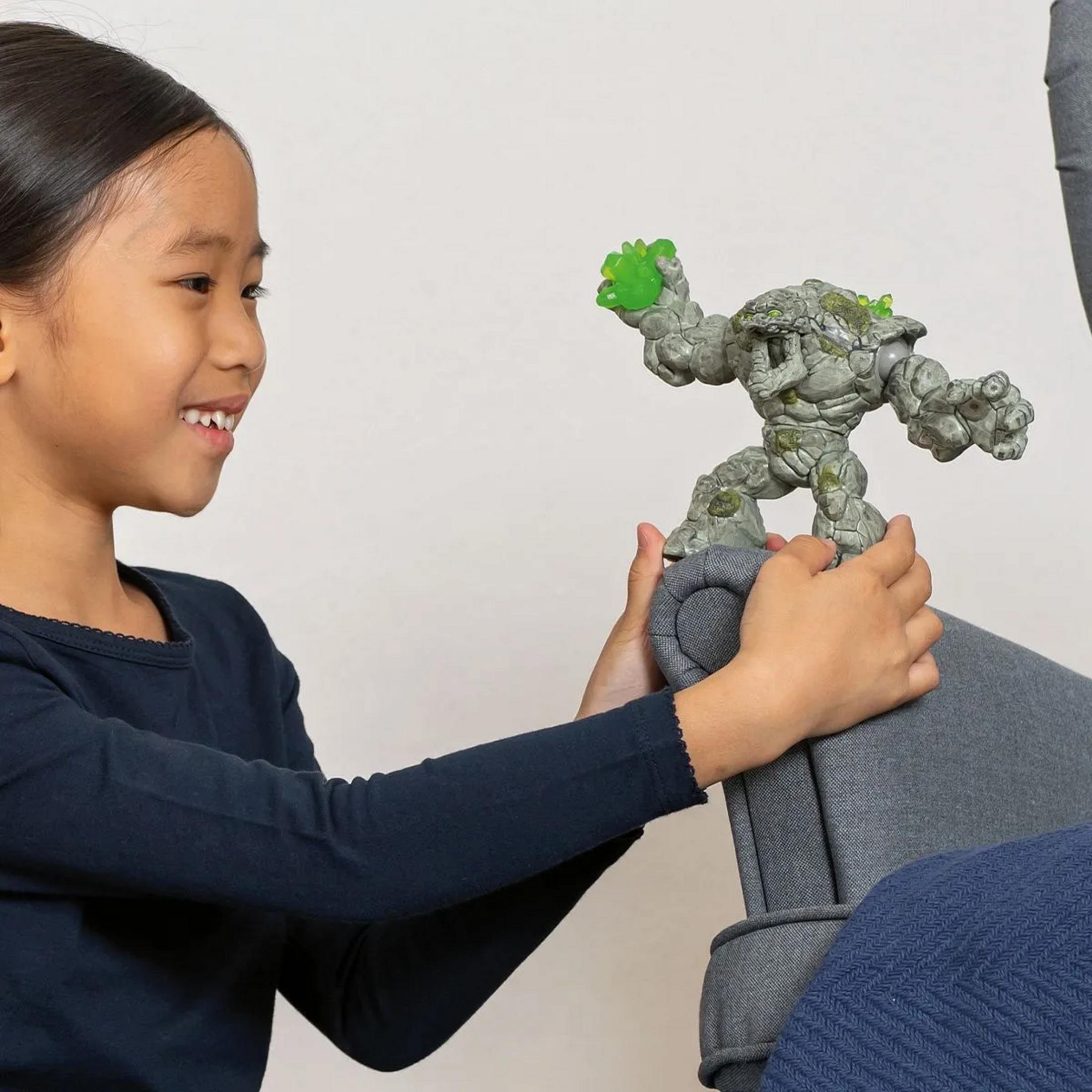 Dziewczynka trzyma kamienną figurkę z zielonymi akcentami na szarej sofie.