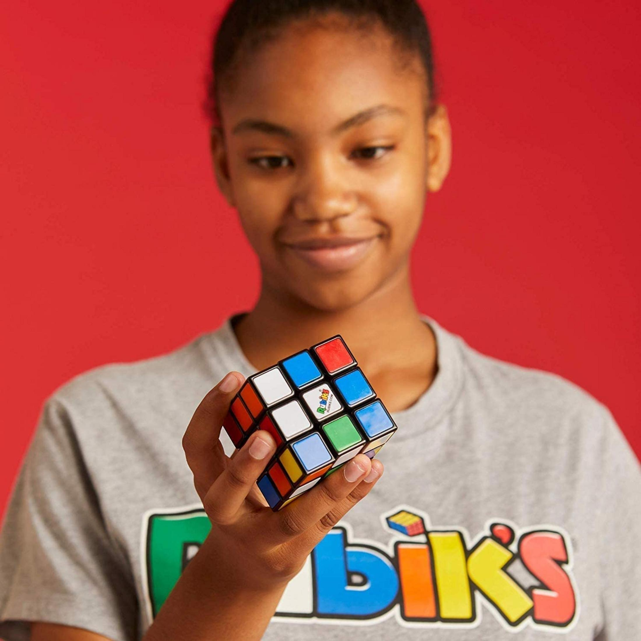 Ein junges Mädchen hält einen Rubik's Cube vor einem roten Hintergrund.