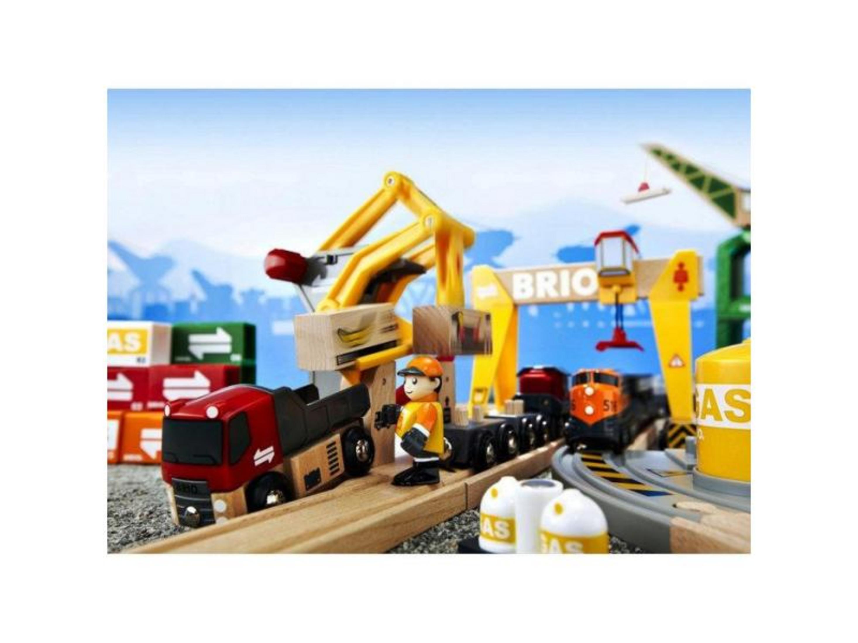 Ein Spielzeug-Güterbahnhof mit Zügen, LKW, Kran und Arbeiterfigur.