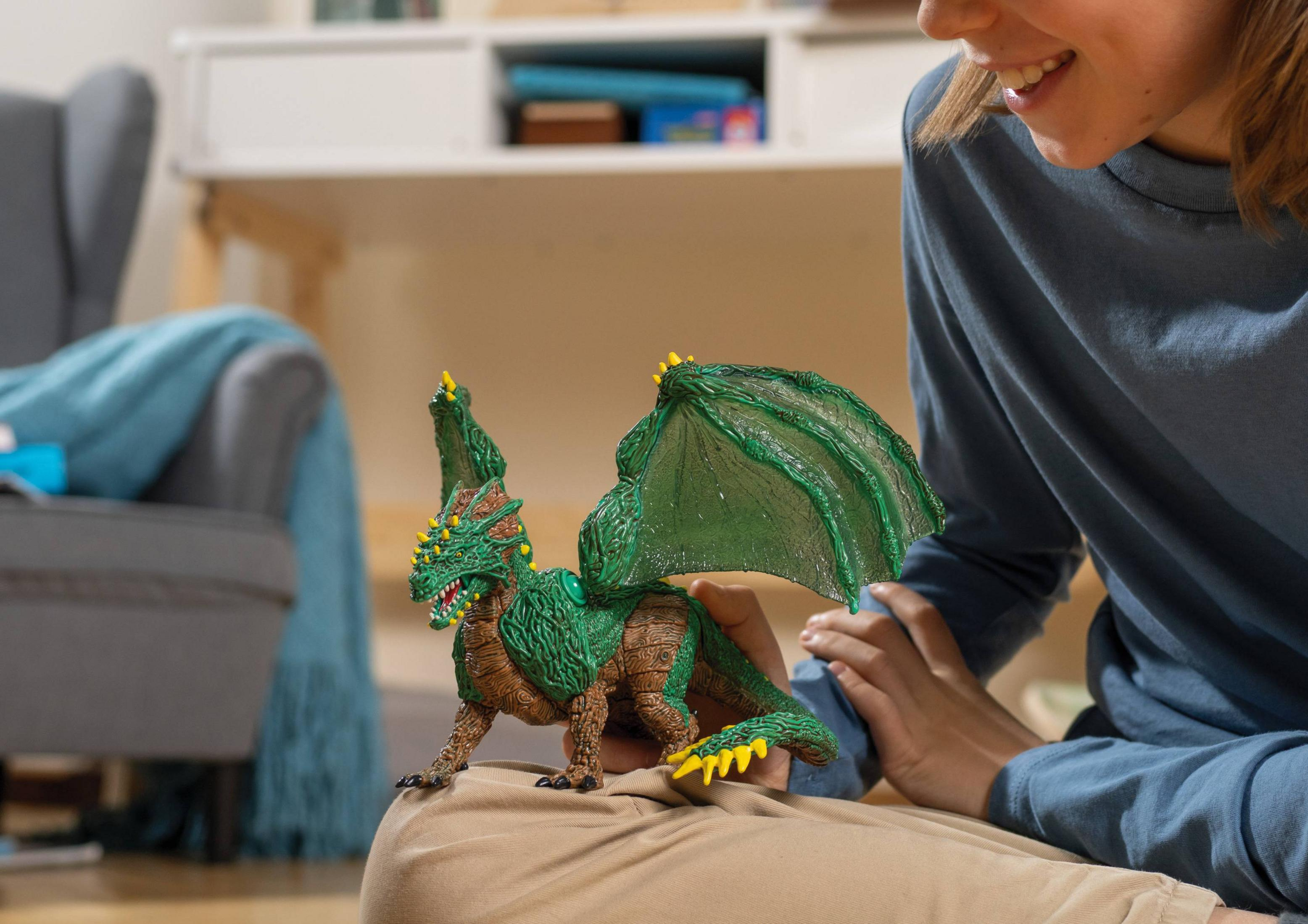 Zielony smok zabawka z żółtymi kolcami, trzymany przez dziecko w niebieskiej koszuli.