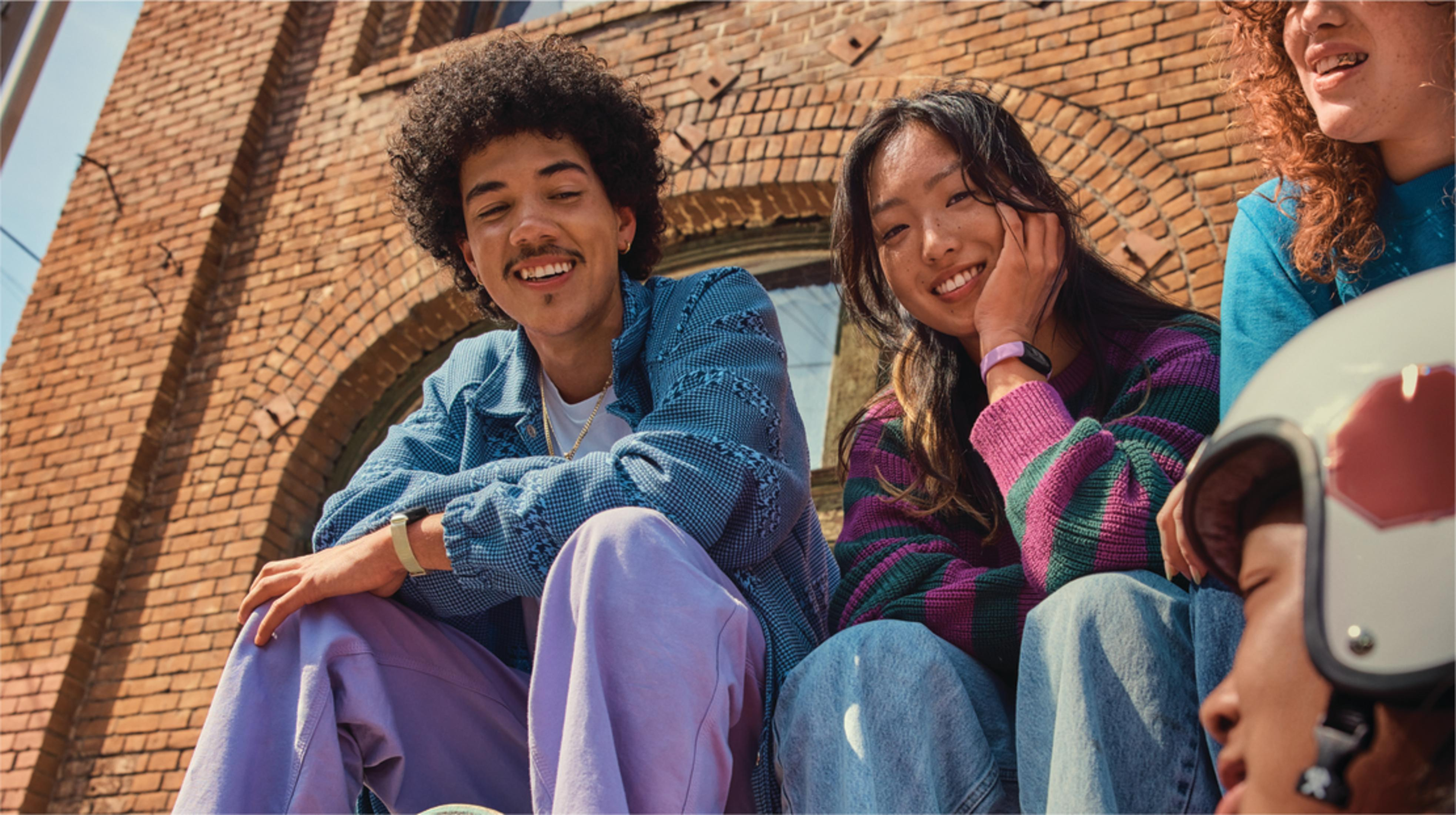 Trzy młode osoby siedzą przed ceglanym murem, uśmiechając się do aparatu.