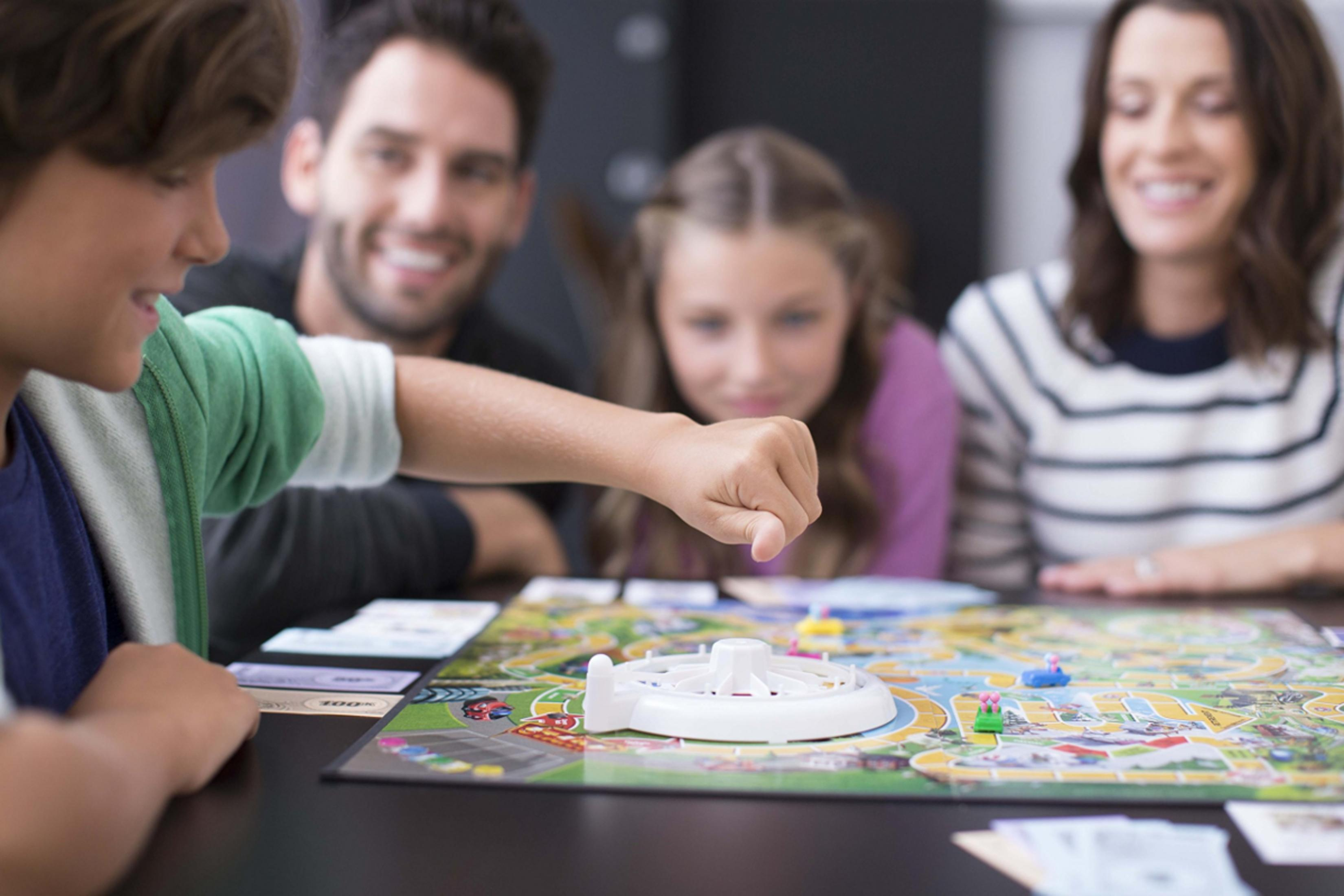 Familie spielt ein Brettspiel mit Autos und Geld.