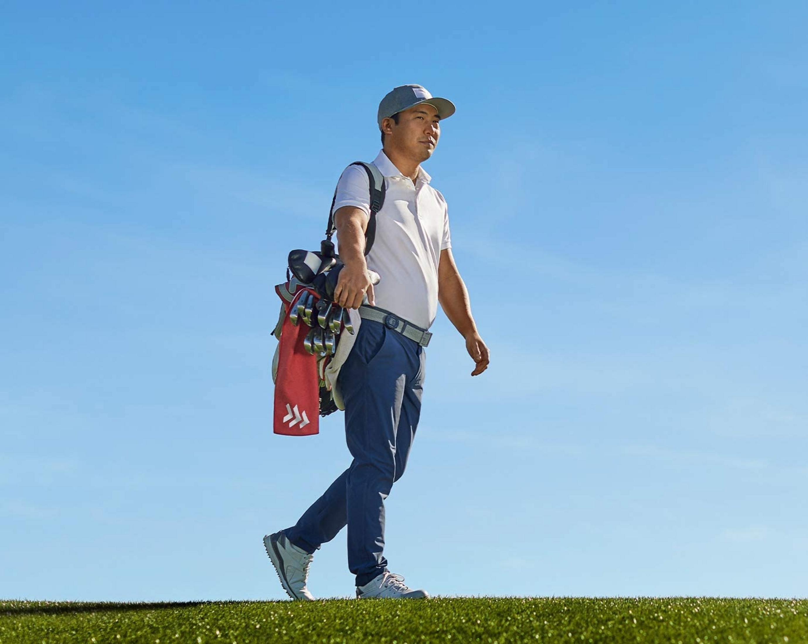 Un hombre con ropa de golf camina sobre césped bajo un cielo azul.