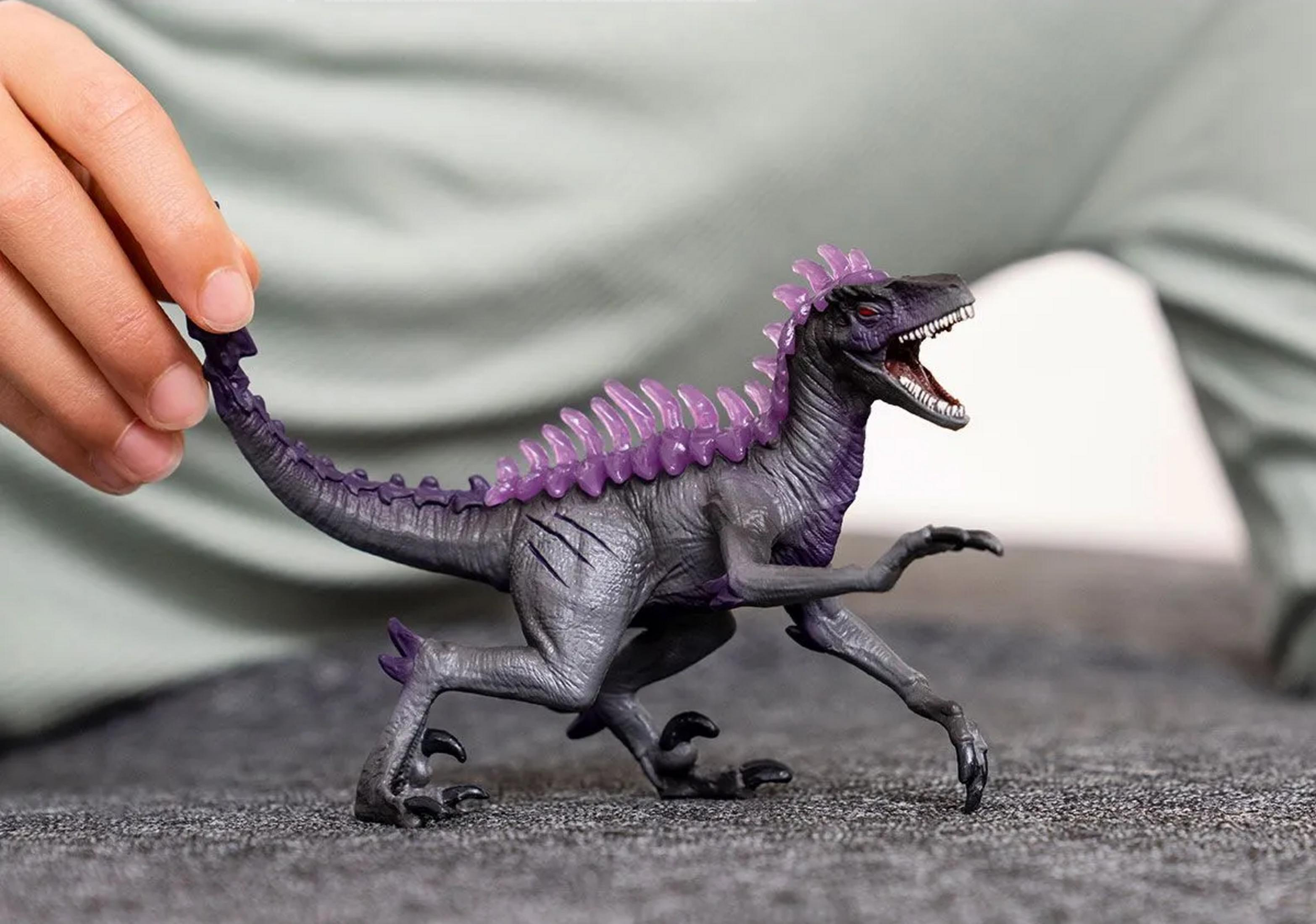 Graue Dinosaurierfigur mit lila Stacheln, gehalten von einer Hand.