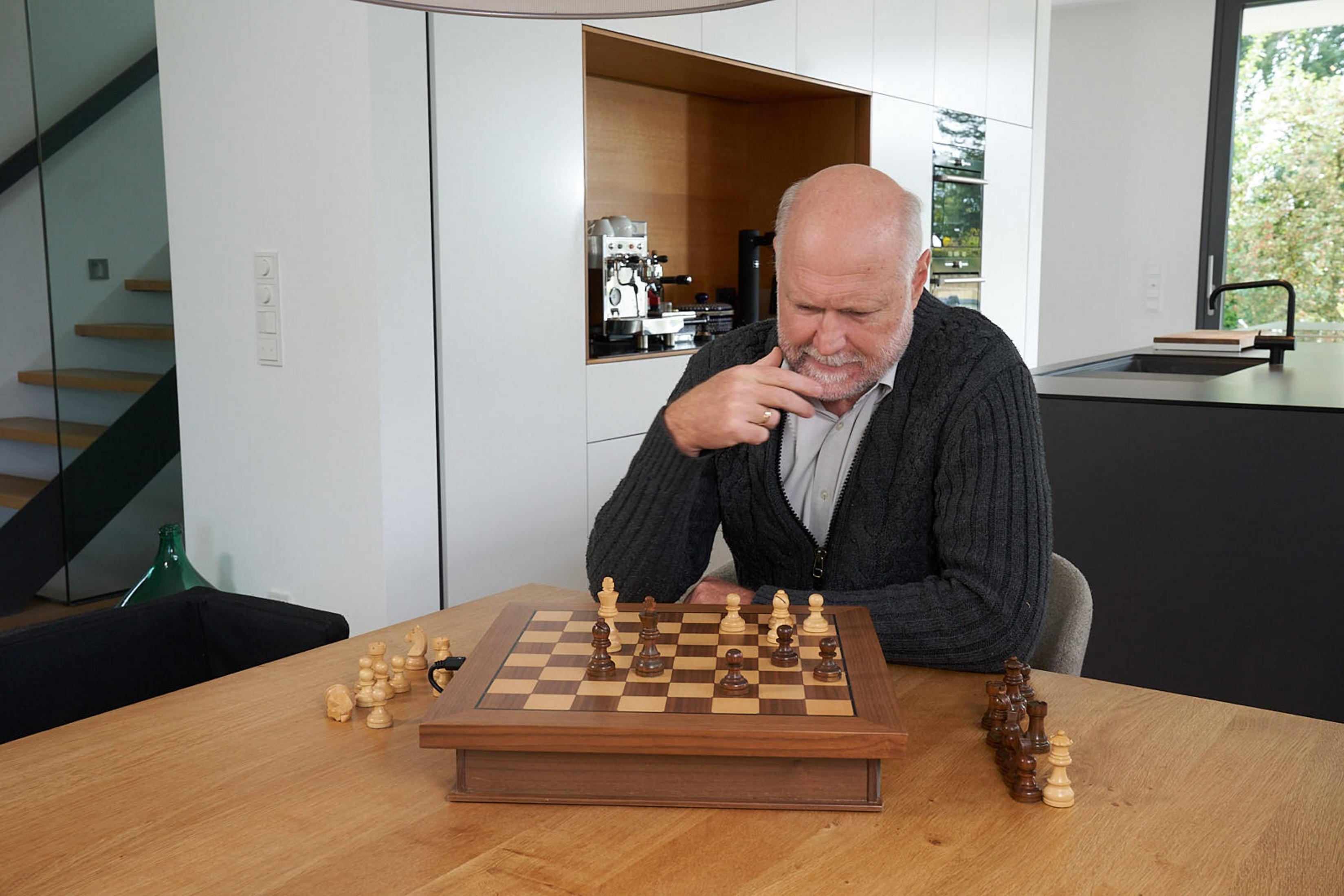 Ein älterer Mann sitzt an einem Holztisch und denkt über ein Schachspiel nach.