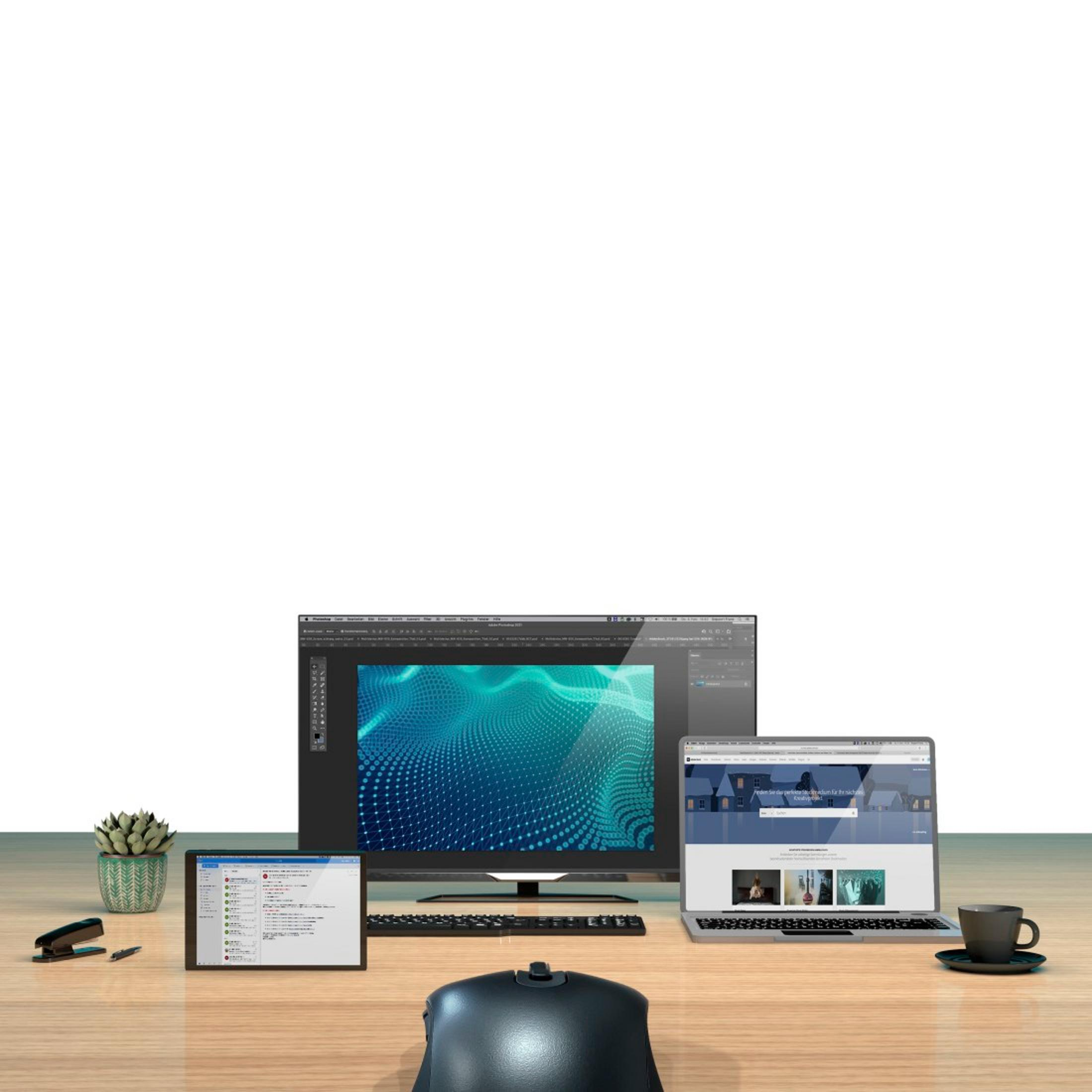 Biurko z trzema ekranami, klawiaturą, myszką, rośliną, zszywaczem i długopisem.