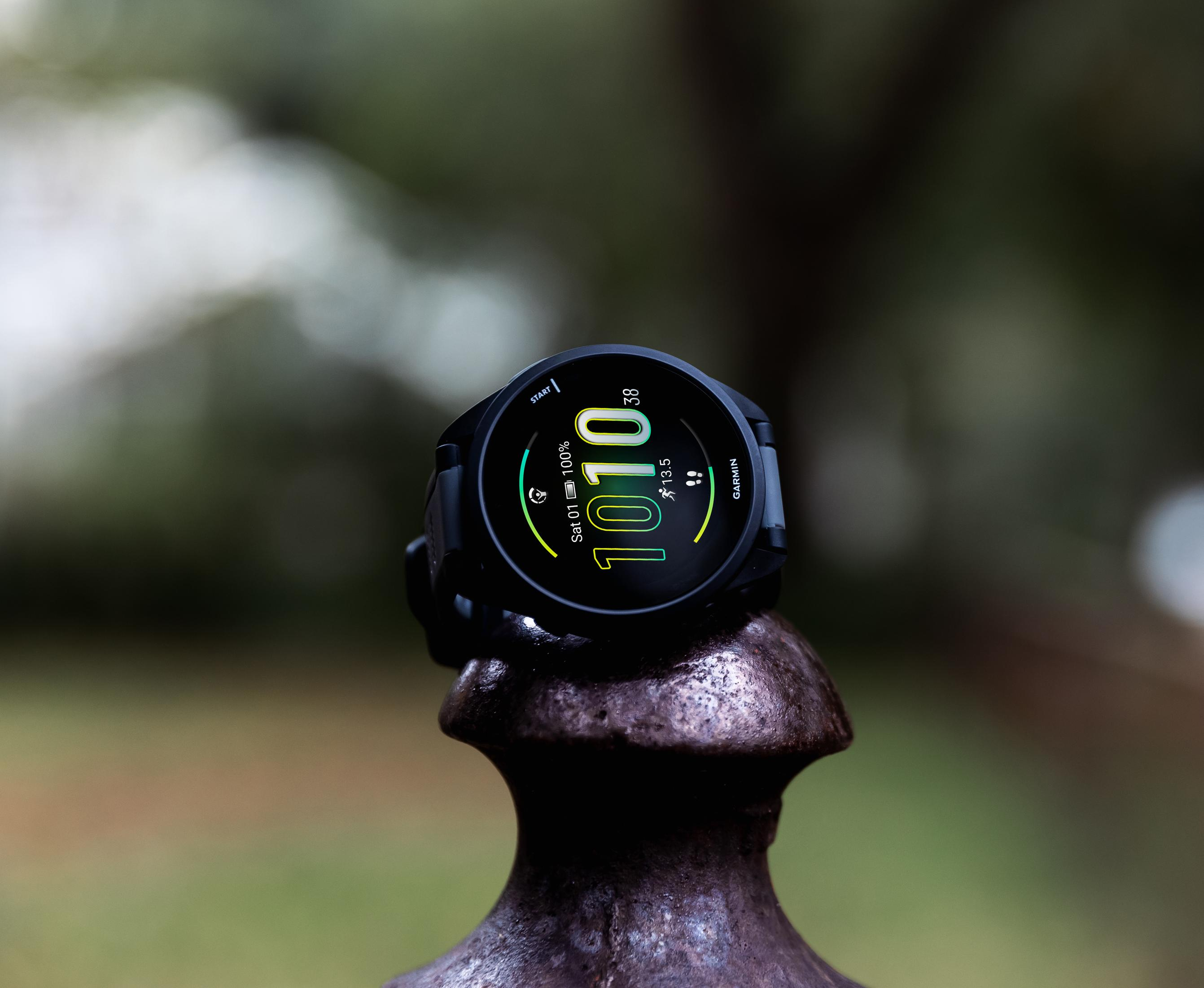 Un reloj inteligente Garmin negro con pantalla verde descansa sobre un soporte de metal oscuro.
