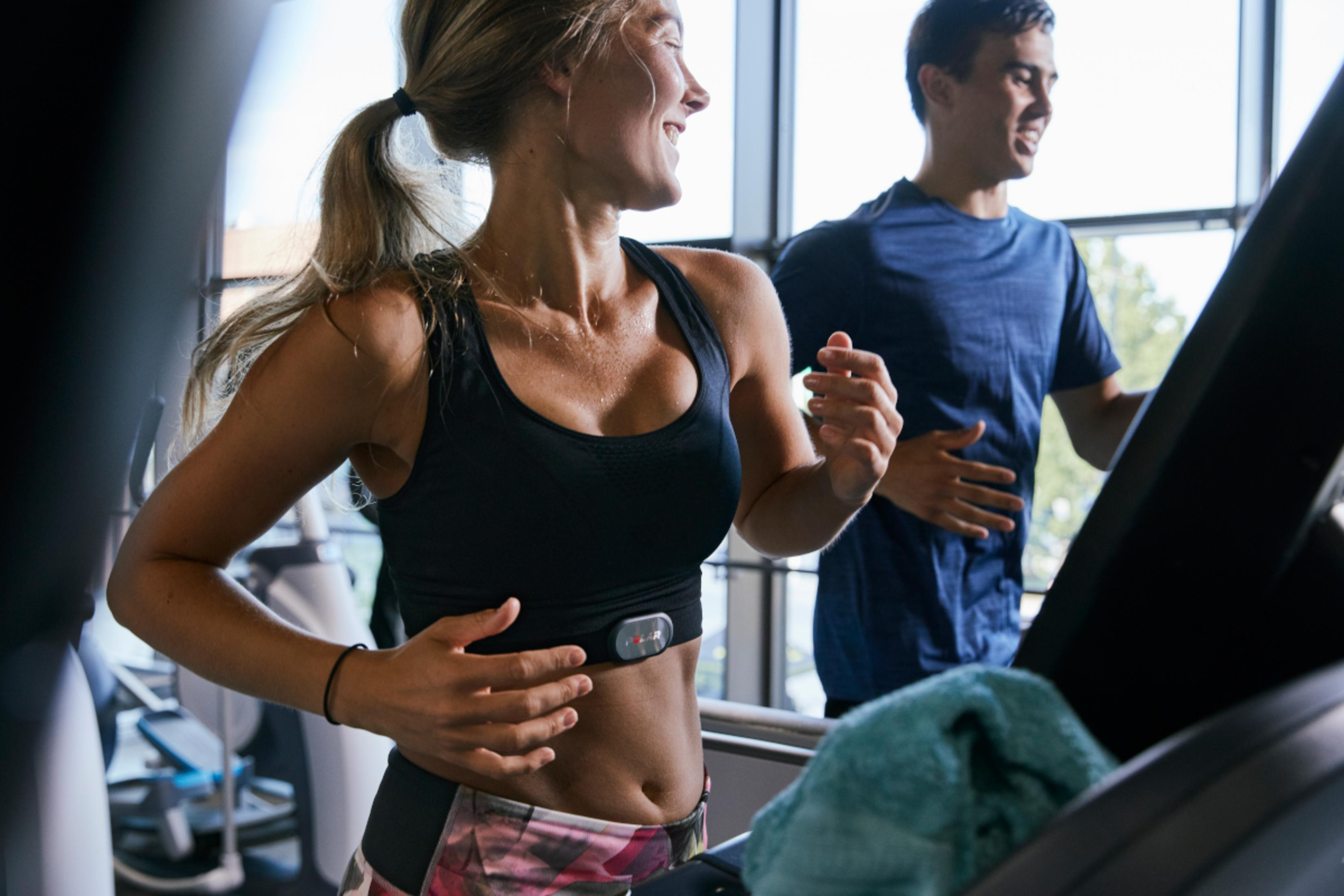 Mężczyzna i kobieta na bieżniach, oboje ćwiczą.