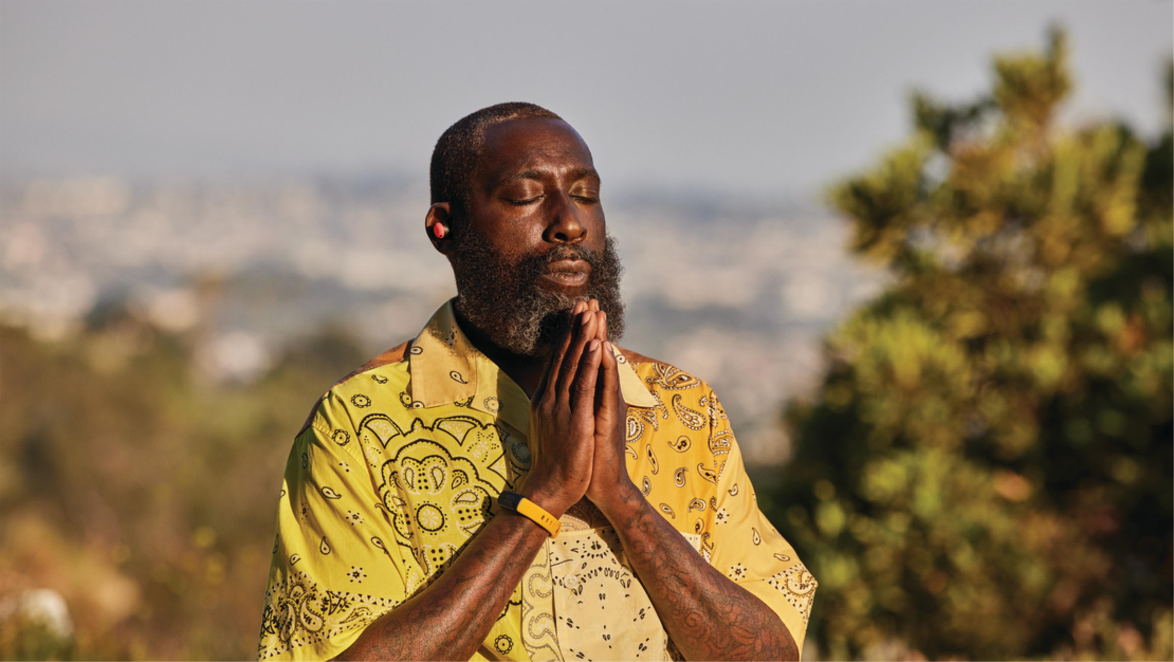 Mężczyzna z brodą modli się z zamkniętymi oczami i złożonymi dłońmi.