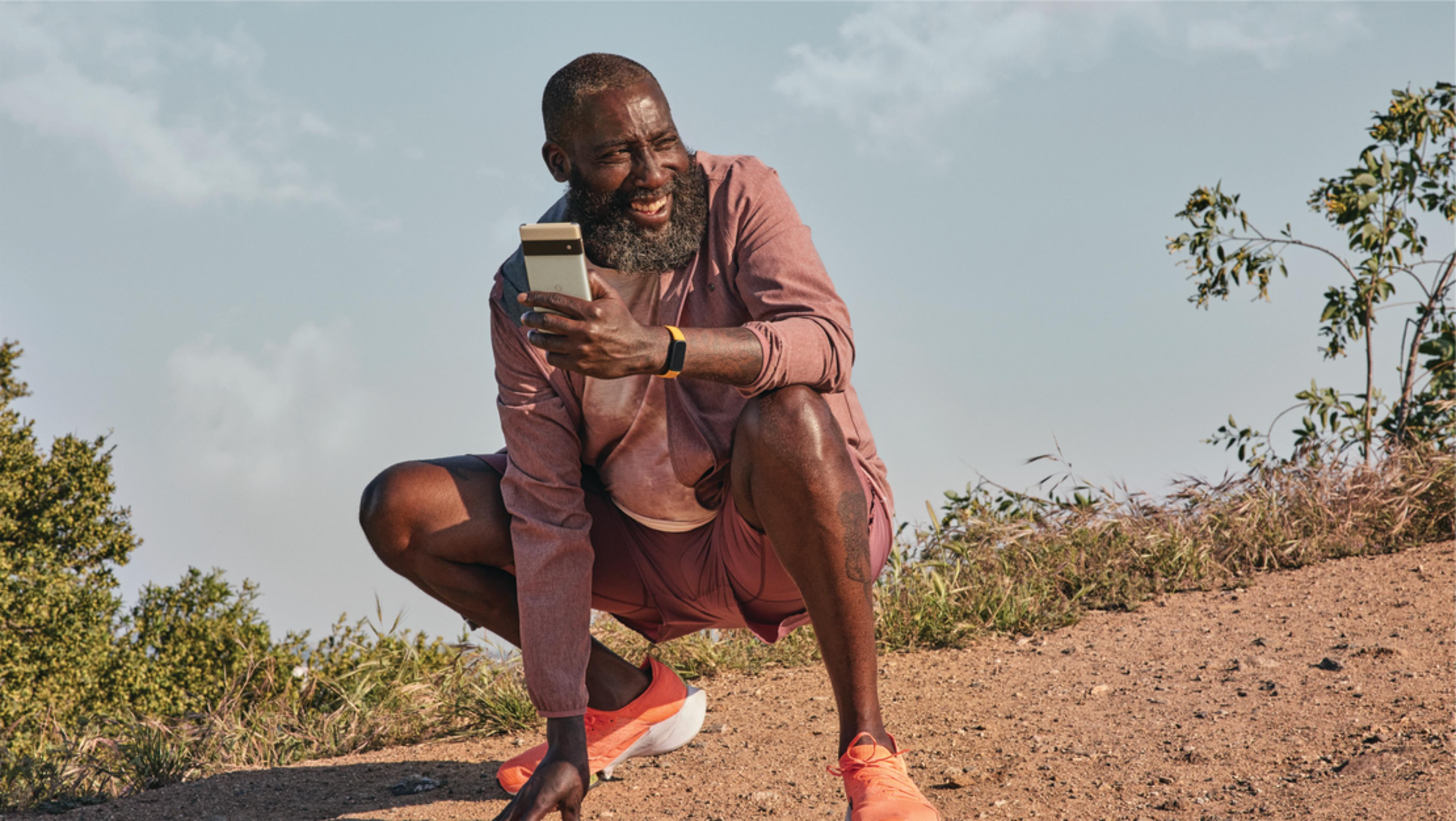 Mężczyzna kuca na zewnątrz, patrząc na telefon.