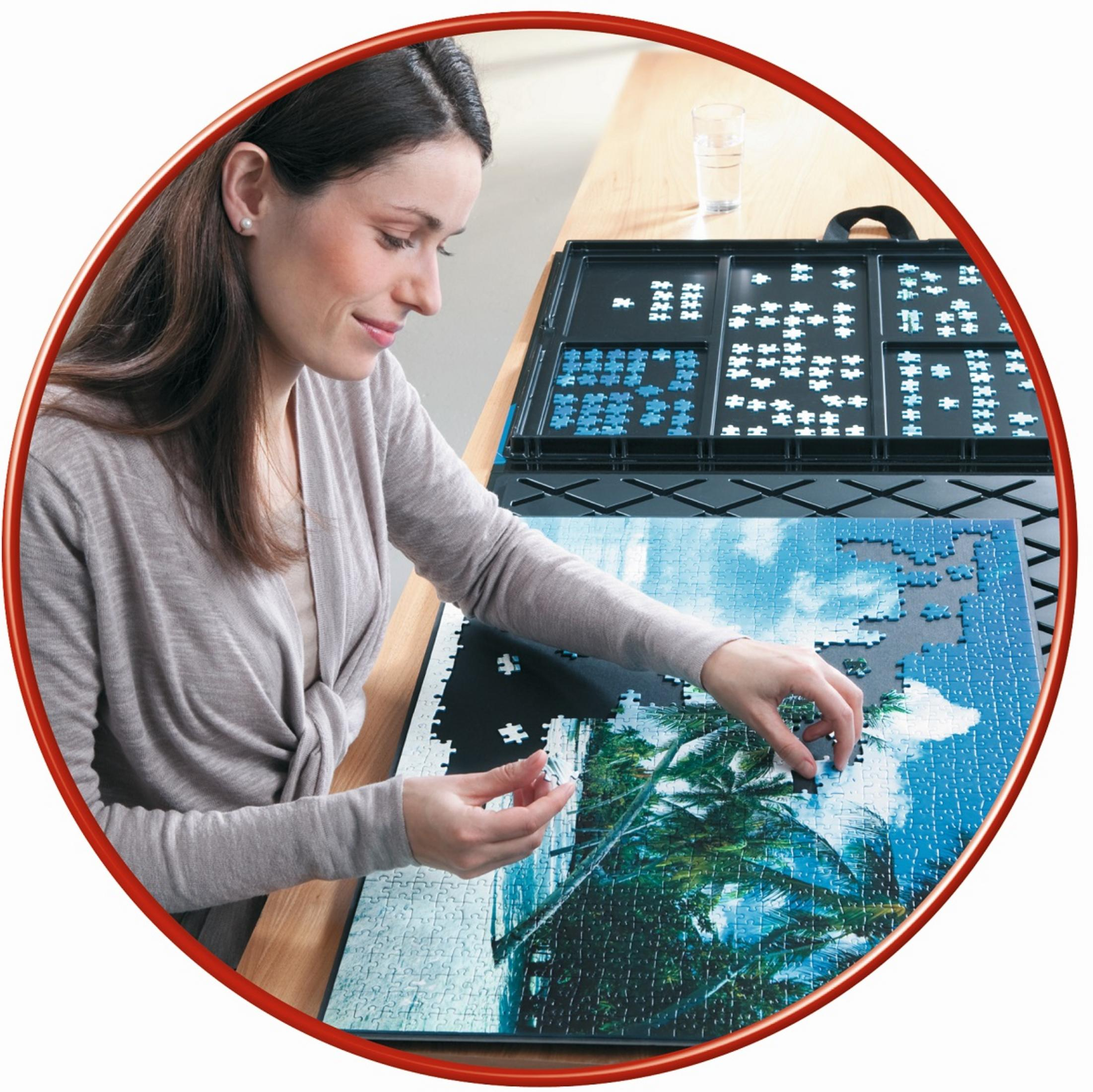 Eine Frau sitzt an einem Tisch und setzt ein Puzzle mit Palmen und blauem Himmel zusammen.