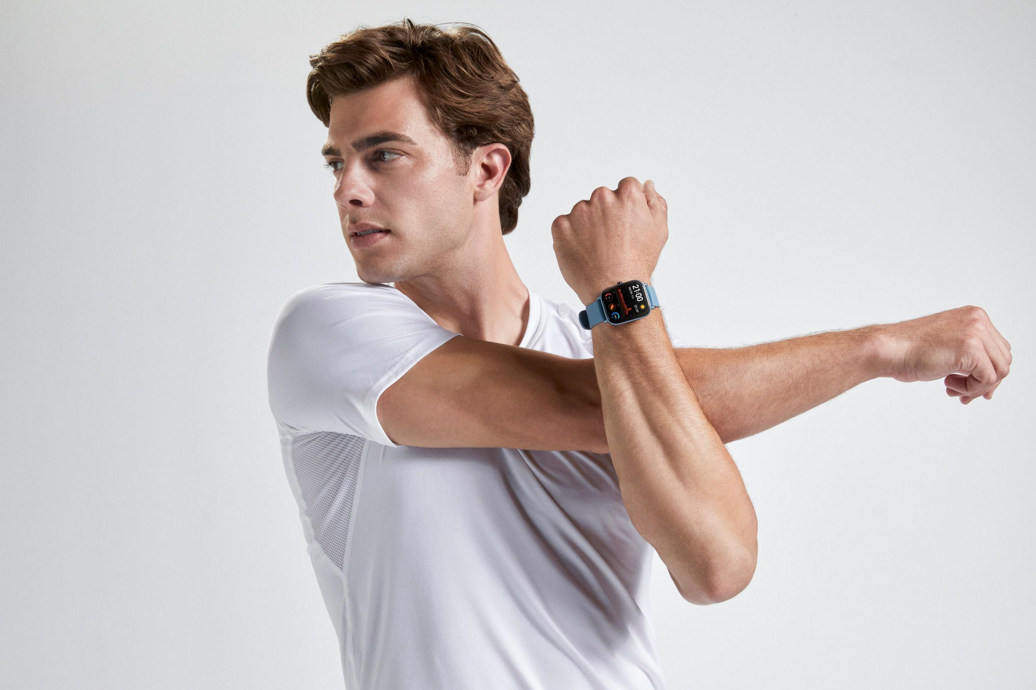 Un uomo in maglietta bianca si allunga. Indossa uno smartwatch blu.