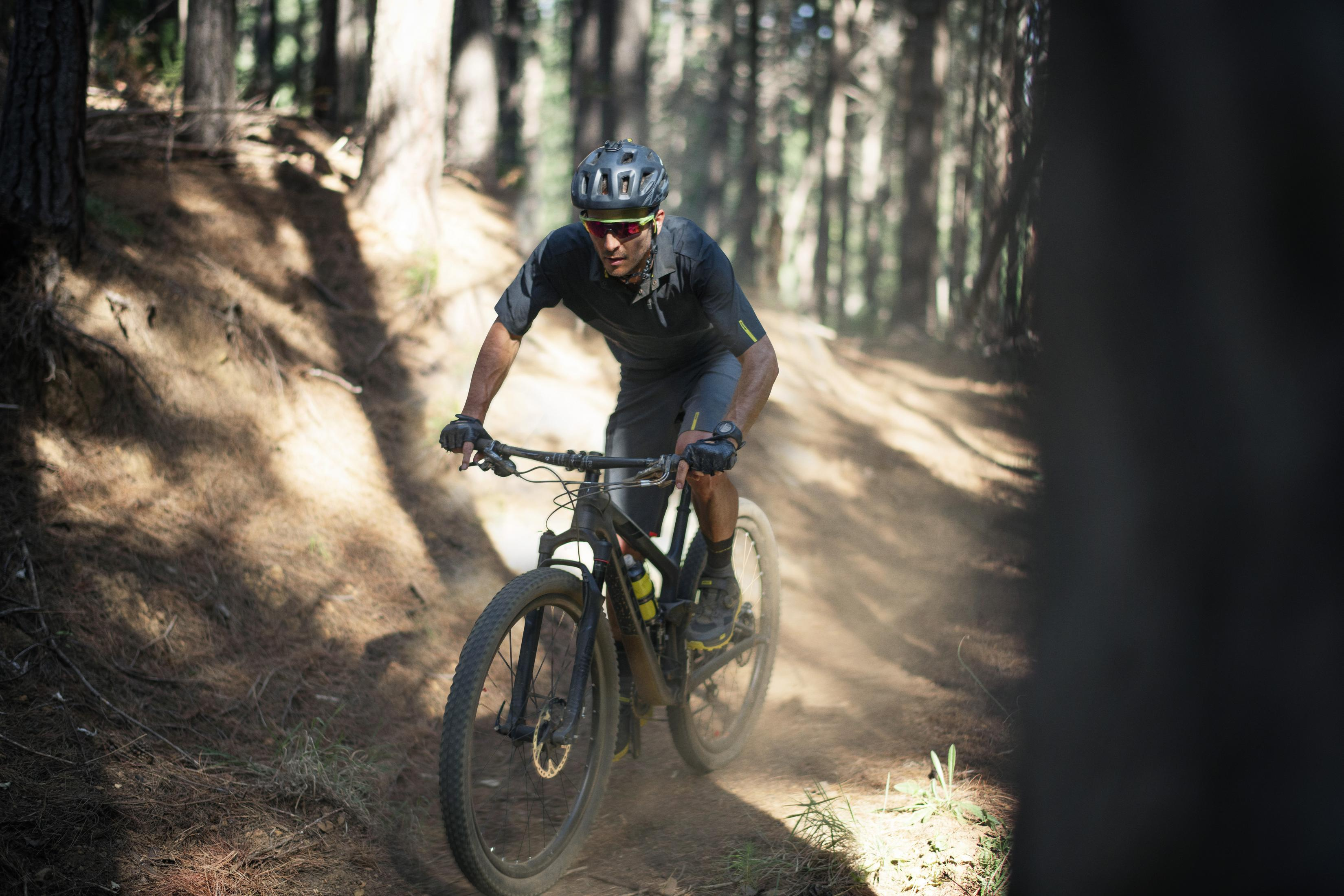 Ein Mann fährt Mountainbike auf einem Waldweg, Staub wirbelt auf.