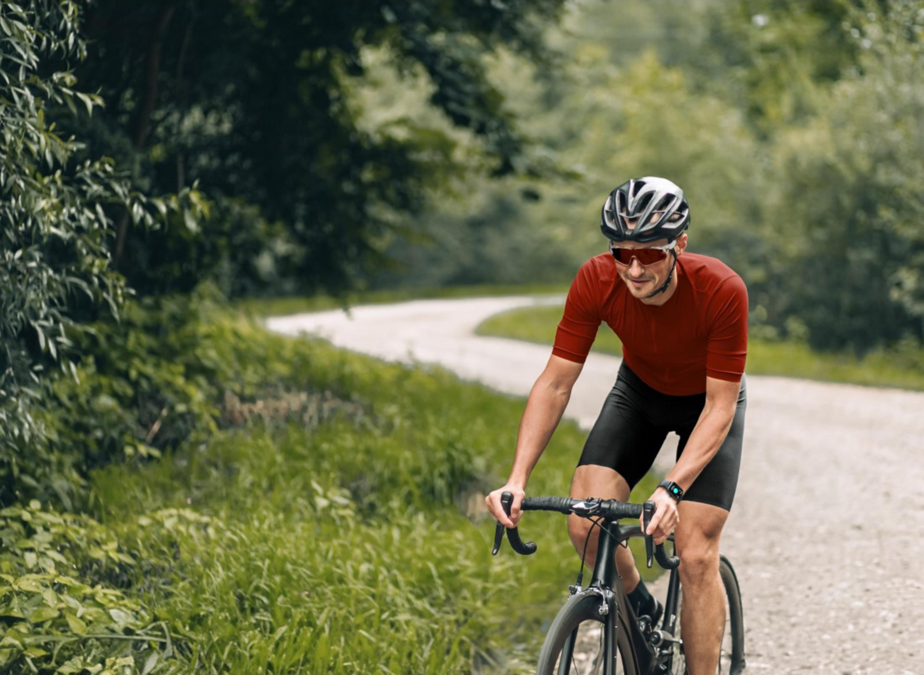 Un uomo in maglia rossa e casco pedala su una strada sterrata.