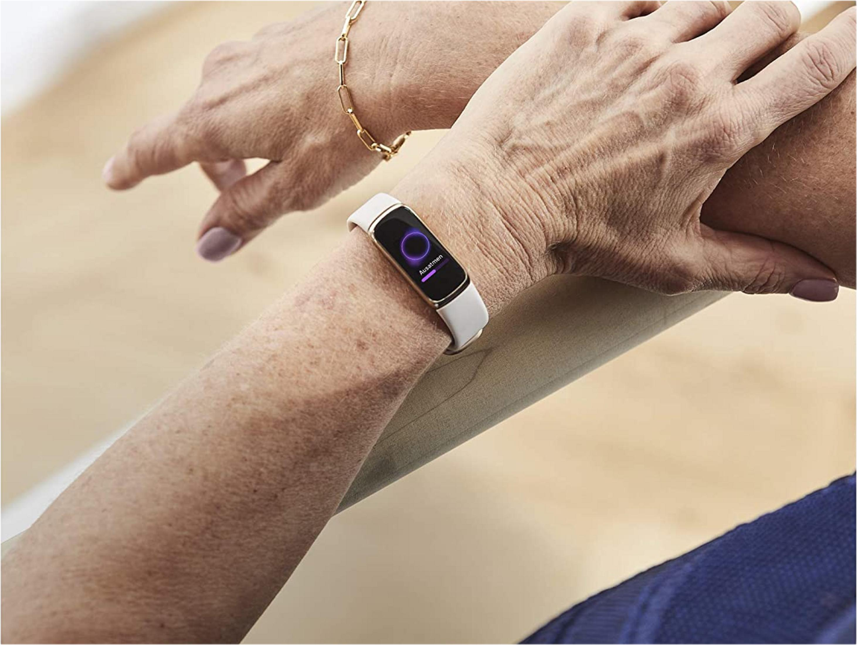 Nahaufnahme der Hände, eine trägt ein weißes Fitnessarmband mit violetter Anzeige.