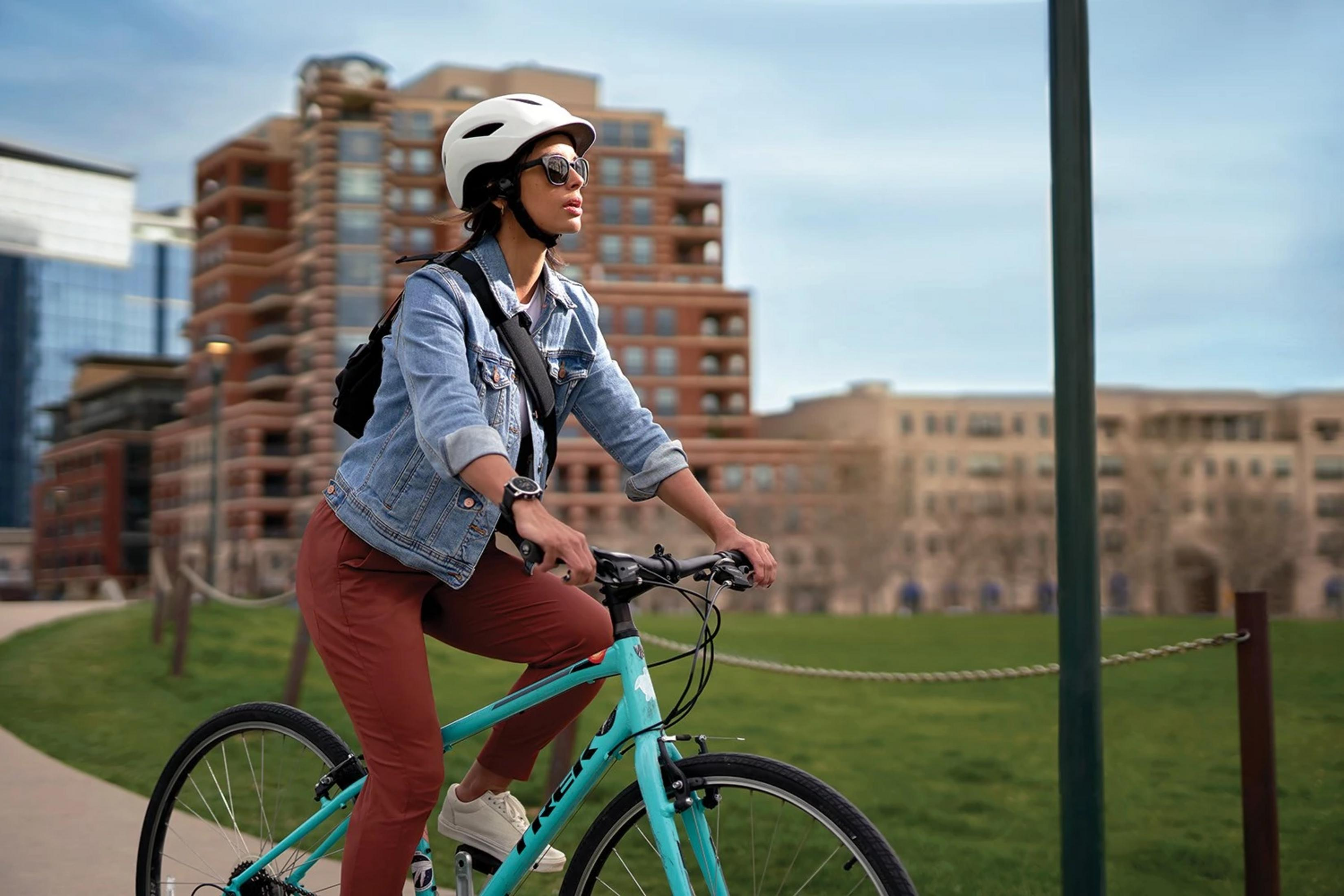 Frau fährt Fahrrad in der Stadt, trägt Helm und Jeansjacke.