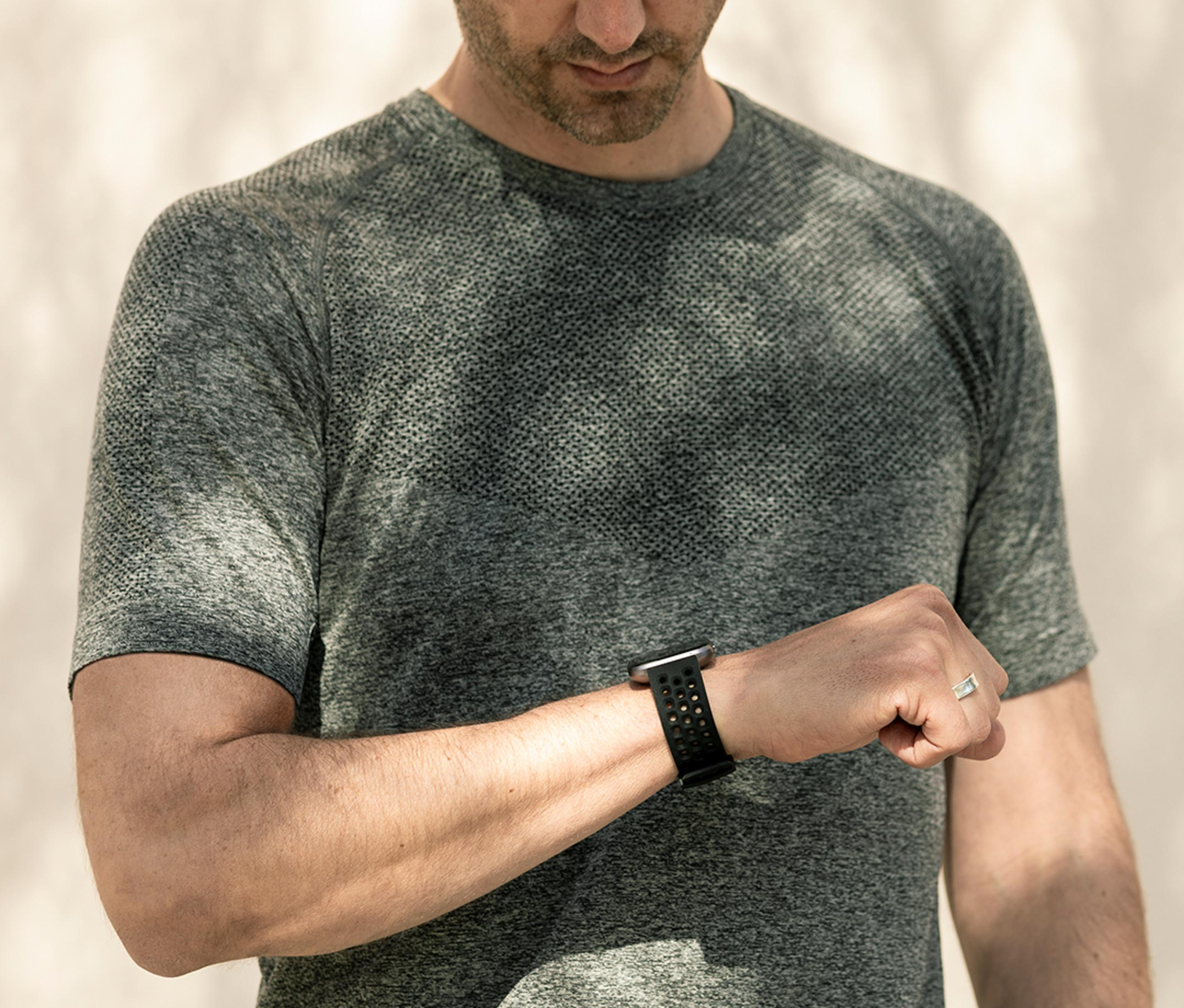 Un hombre con camiseta gris mira su smartwatch. Lleva un anillo en el dedo.