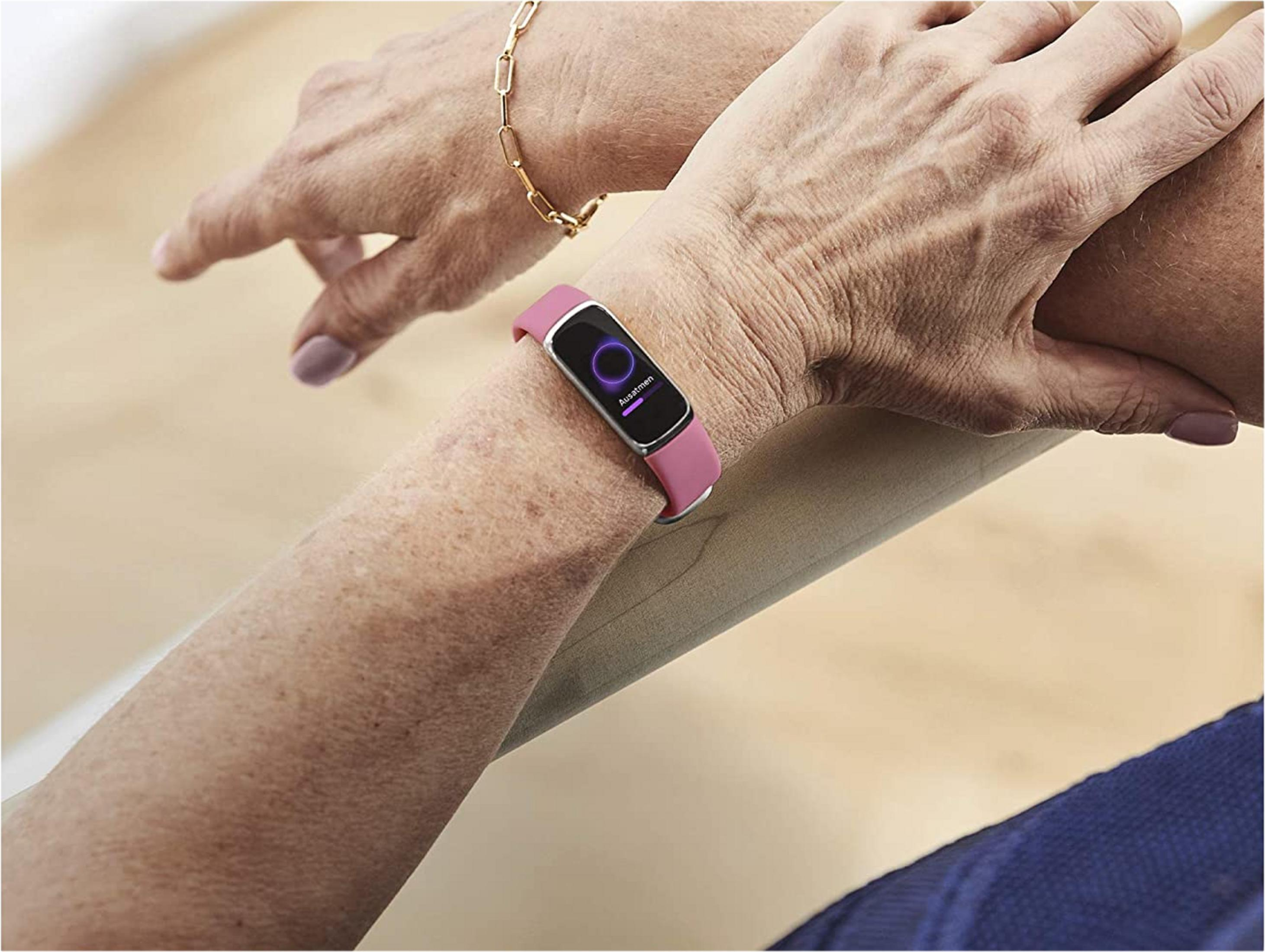 Eine Person trägt ein rosa Fitnessarmband mit einem violetten Kreis und Text.