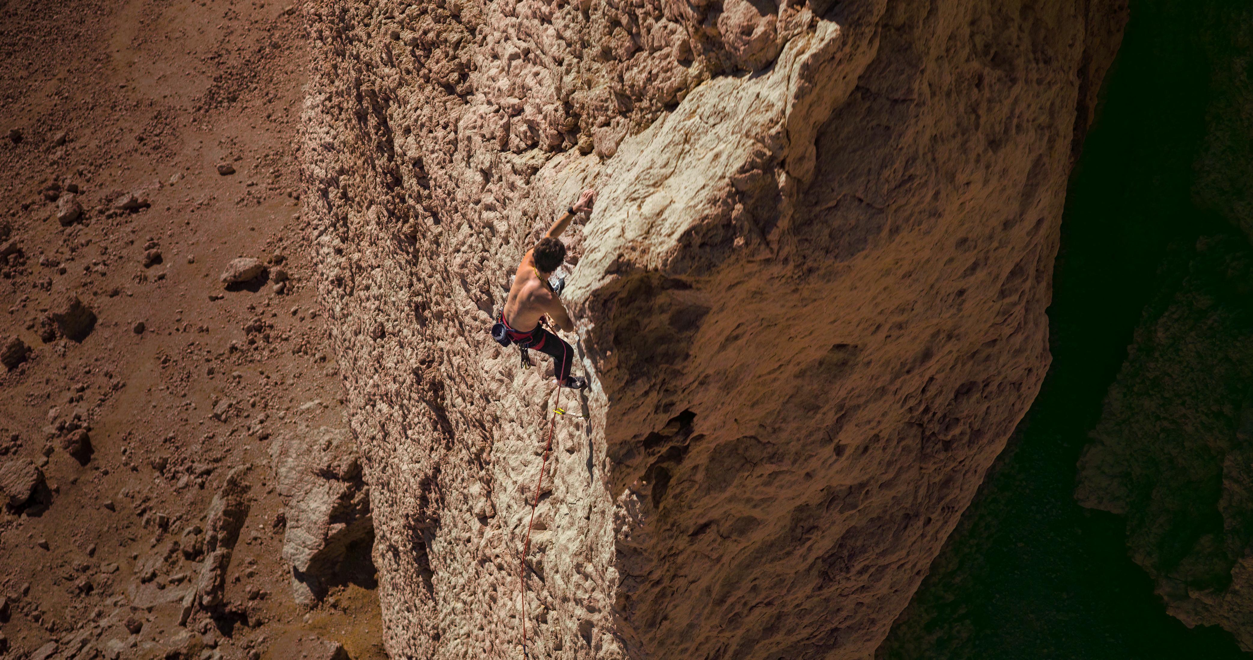 Mężczyzna wspina się po skale. Teren jest suchy i kamienisty z ciemnymi cieniami.