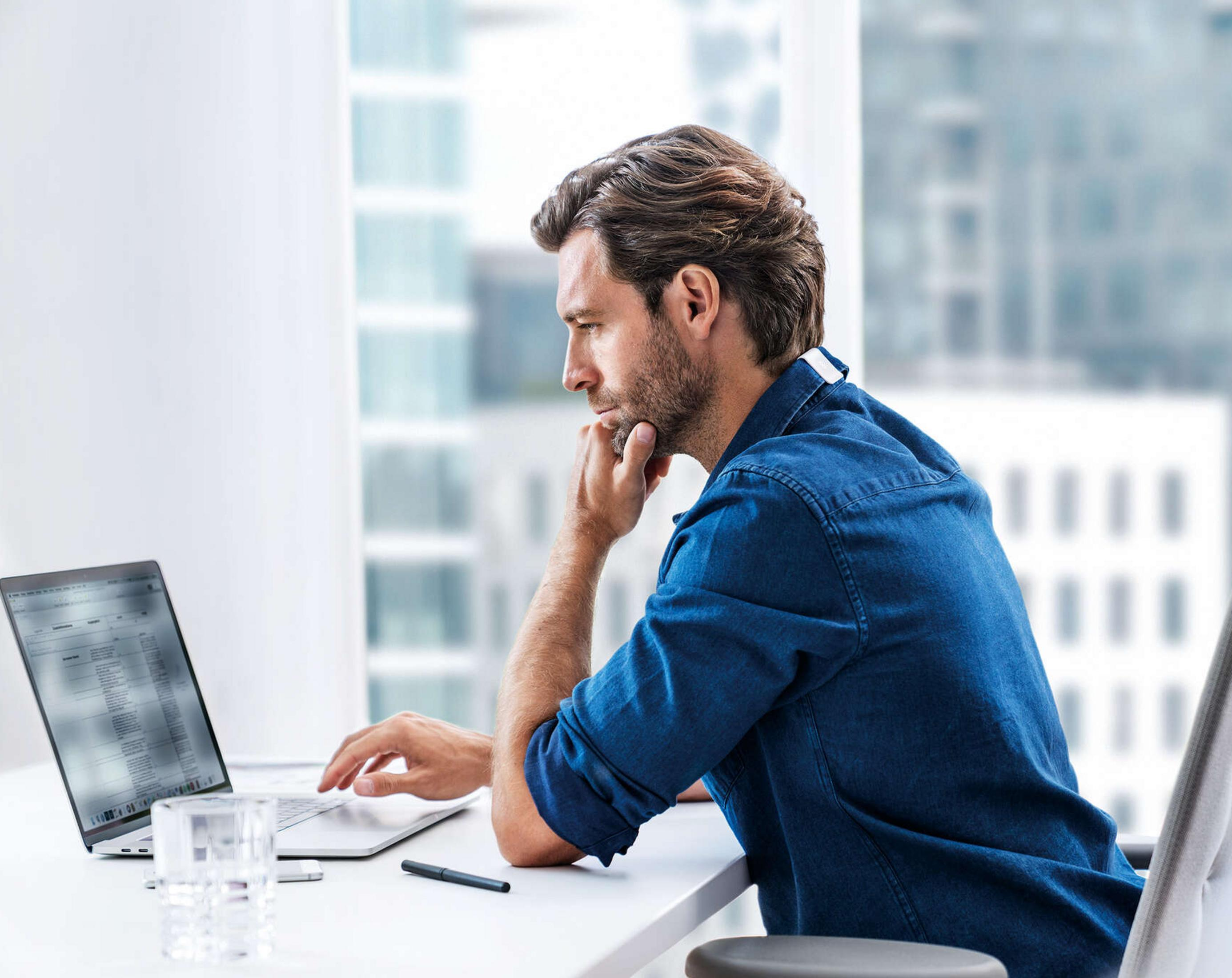 Mann in Jeanshemd arbeitet am Laptop, sitzt am Schreibtisch.