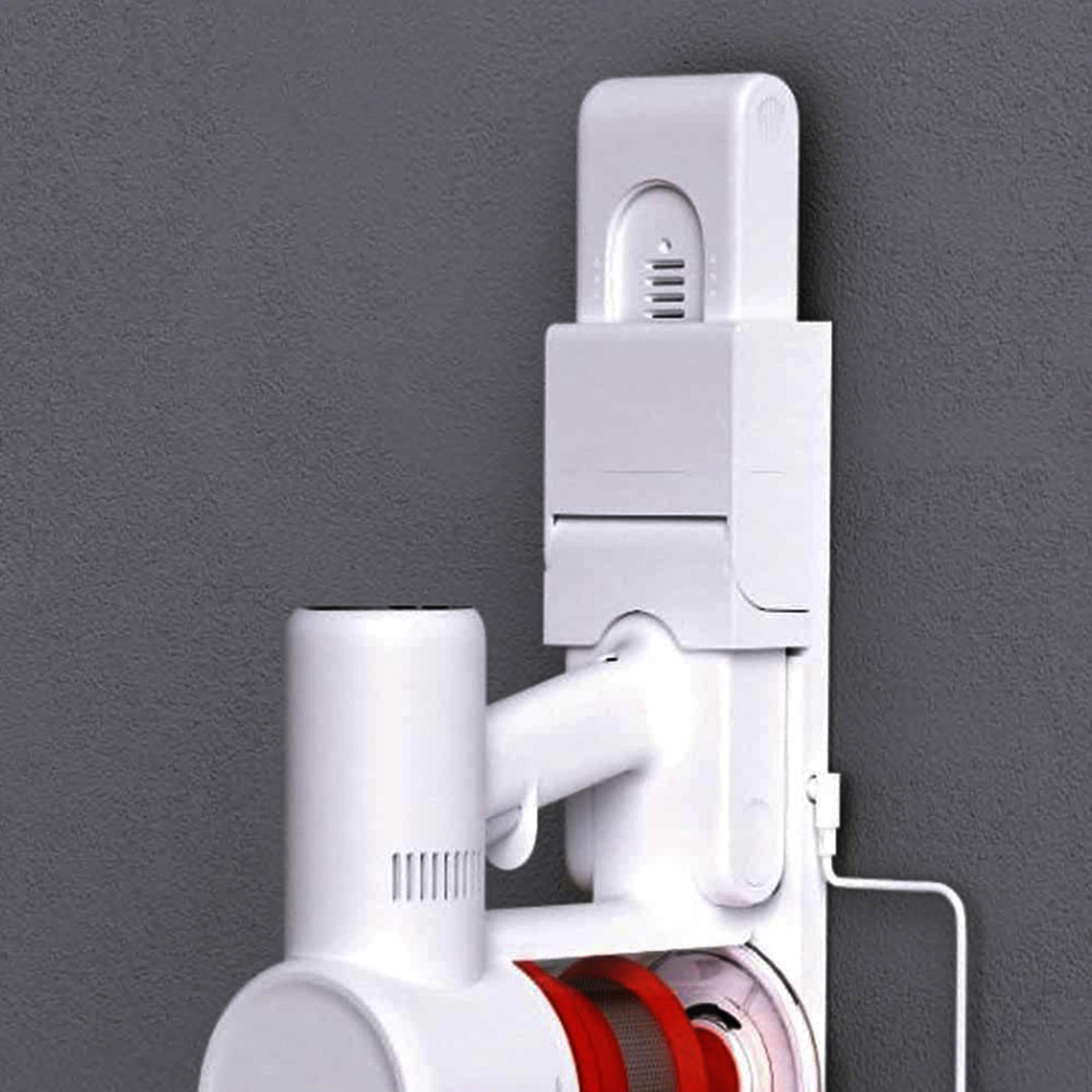 Biały odkurzacz bezprzewodowy z czerwonymi detalami wisi na szarej ścianie.