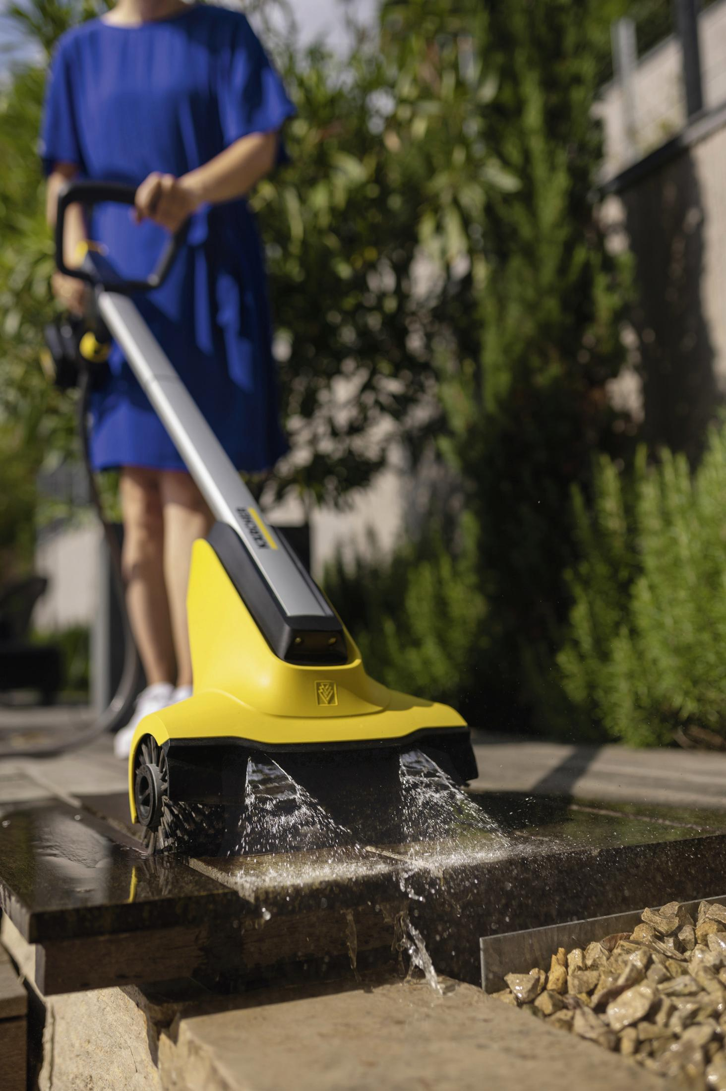 Eine Person reinigt mit einem gelben Gerät einen Steinweg. Wasser spritzt.